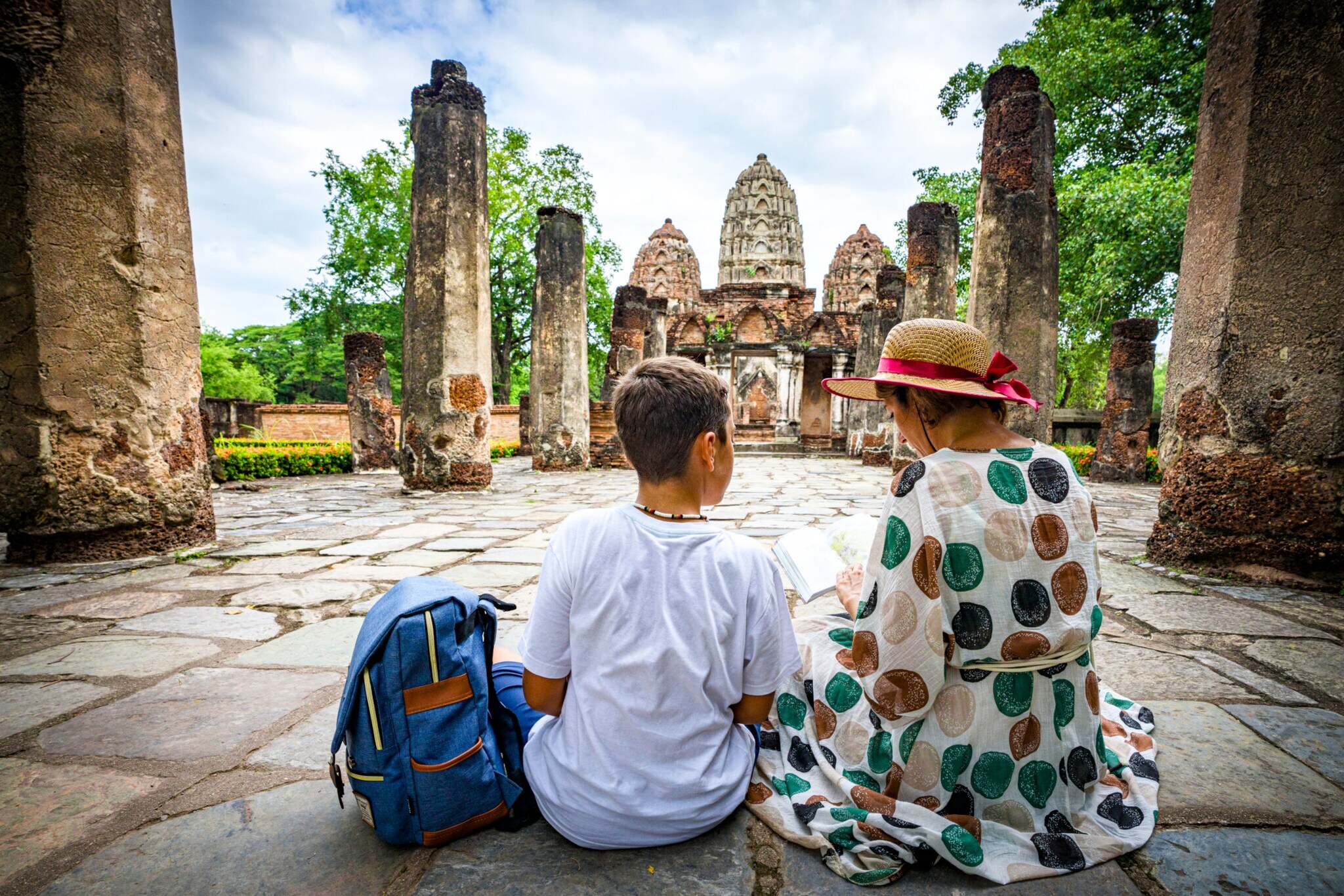 Eine Frau sitzt mit einem Jungen auf Steinen mitten in der thailändischen Tempelanlage Wat Mahathat.