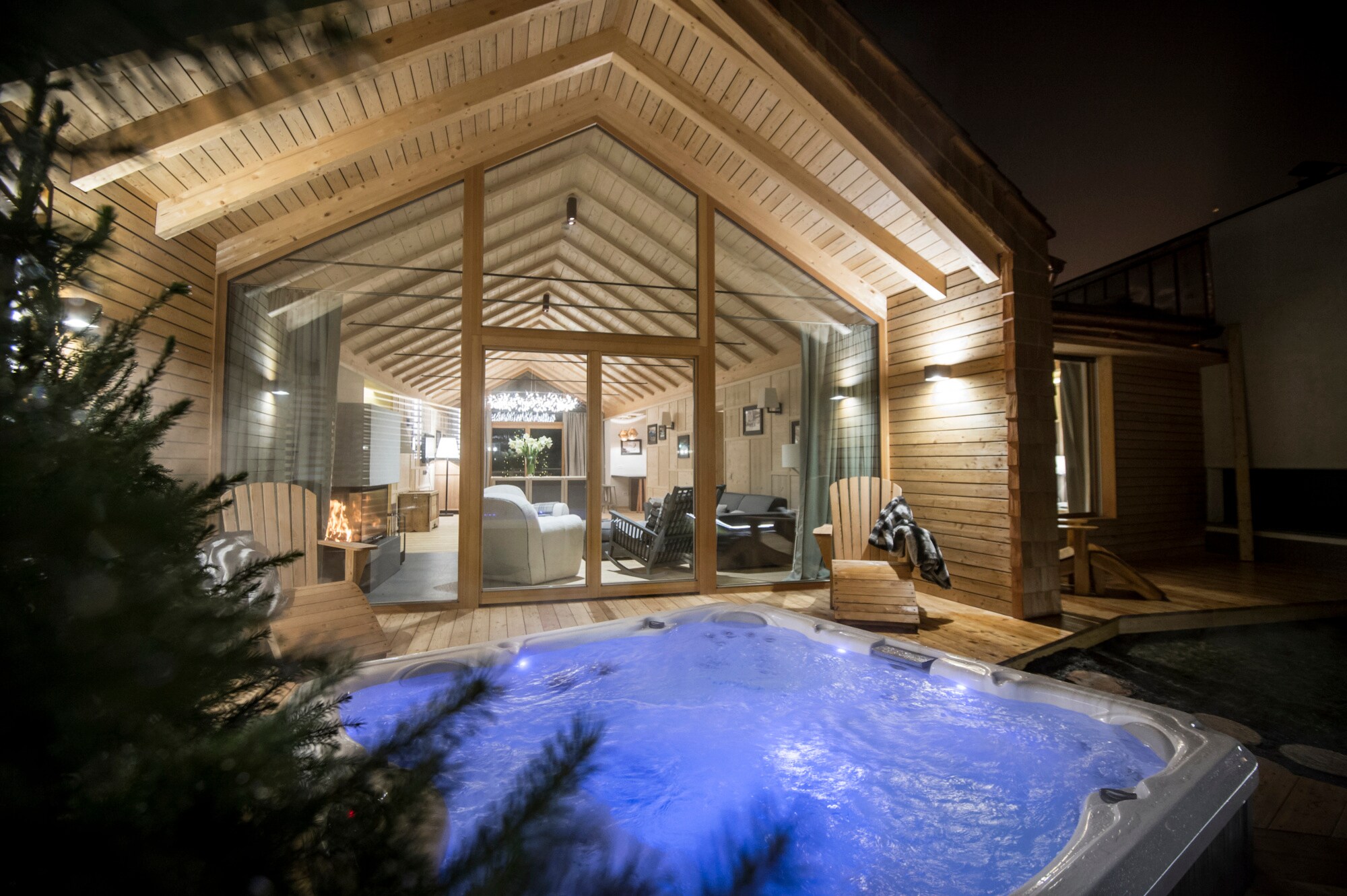 Ein beleuchteter Jacuzzi vor einem Chalet mit großen Holzfenstern Ein beleuchteter Jacuzzi vor einem Chalet mit großen Holzfenstern