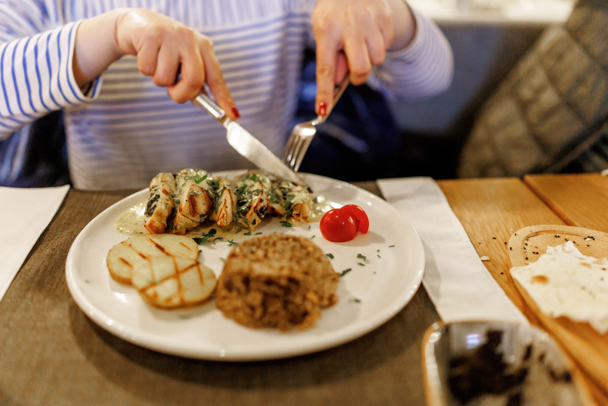 Hände einer Frau, die mit Messer und Gabel ein Gericht von einem weißen Teller isst. Hände einer Frau, die mit Messer und Gabel ein Gericht von einem weißen Teller isst.