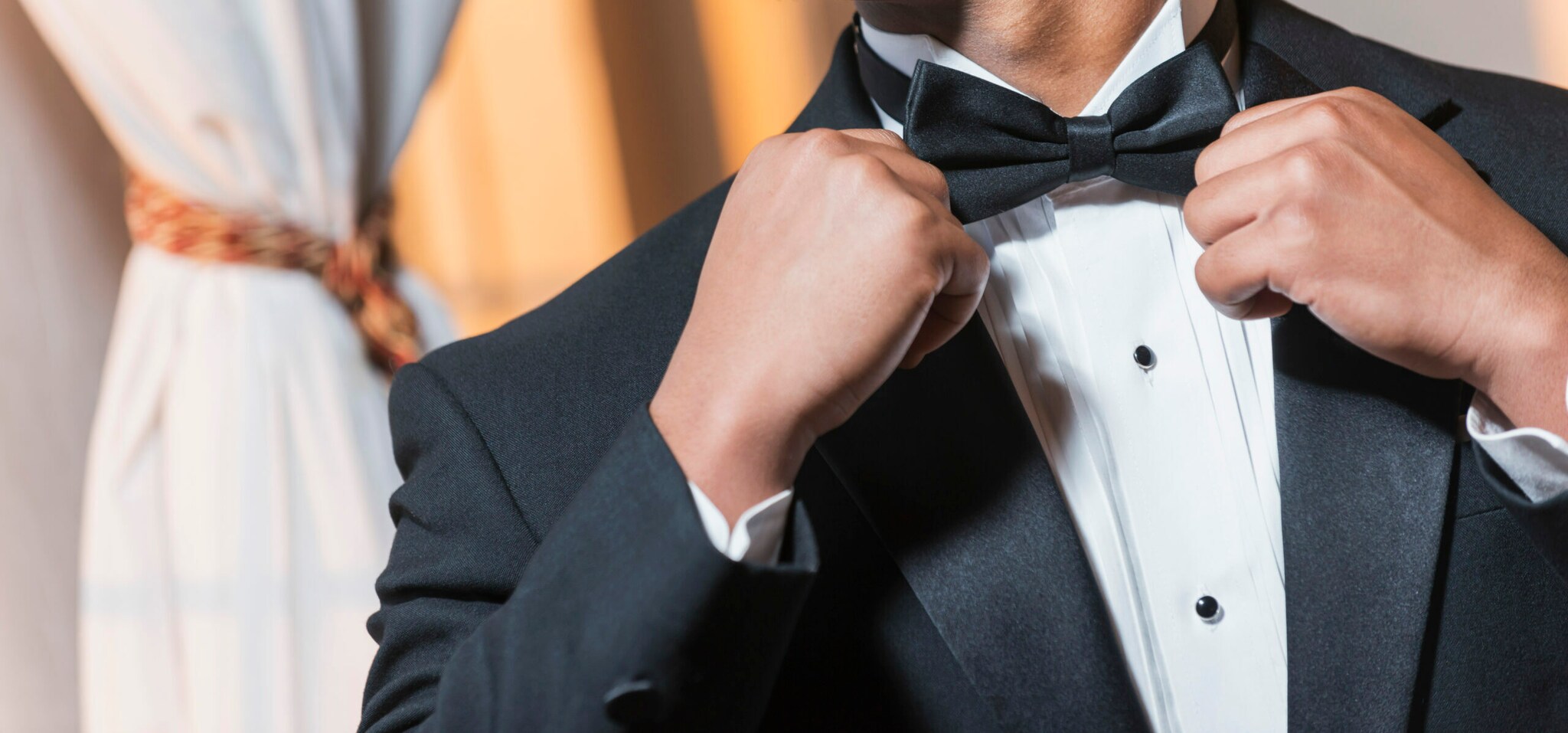 Ein lächelnder Mann im weißen Hemd legt eine schwarze Fliege an