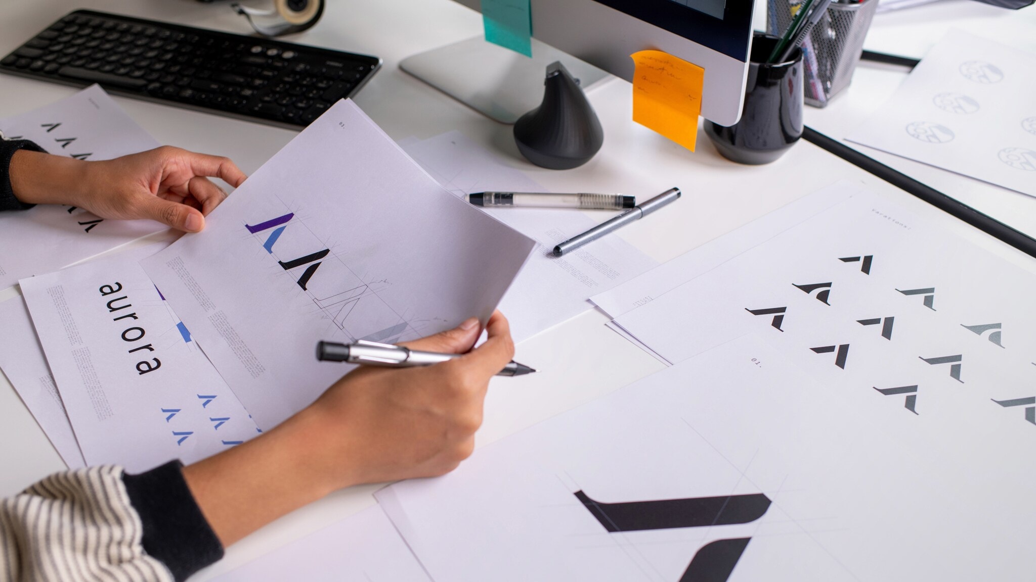 Entwurfsgestaltung eines Logos auf Papierblättern in den Händen einer Person auf einem Schreibtisch. Entwurfsgestaltung eines Logos auf Papierblättern in den Händen einer Person auf einem Schreibtisch.