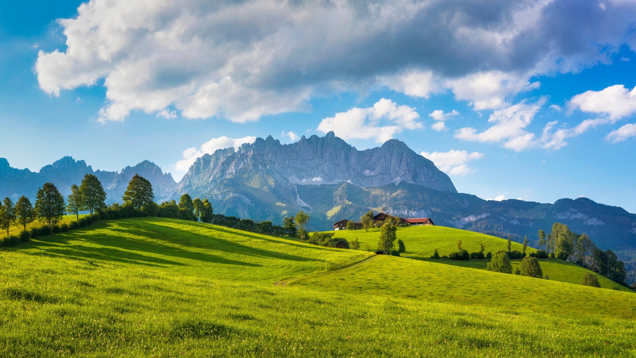 Blick auf ein markantes Gebirge, im Vordergrund eine grüne Wiese mit Bäumen. Blick auf ein markantes Gebirge, im Vordergrund eine grüne Wiese mit Bäumen.