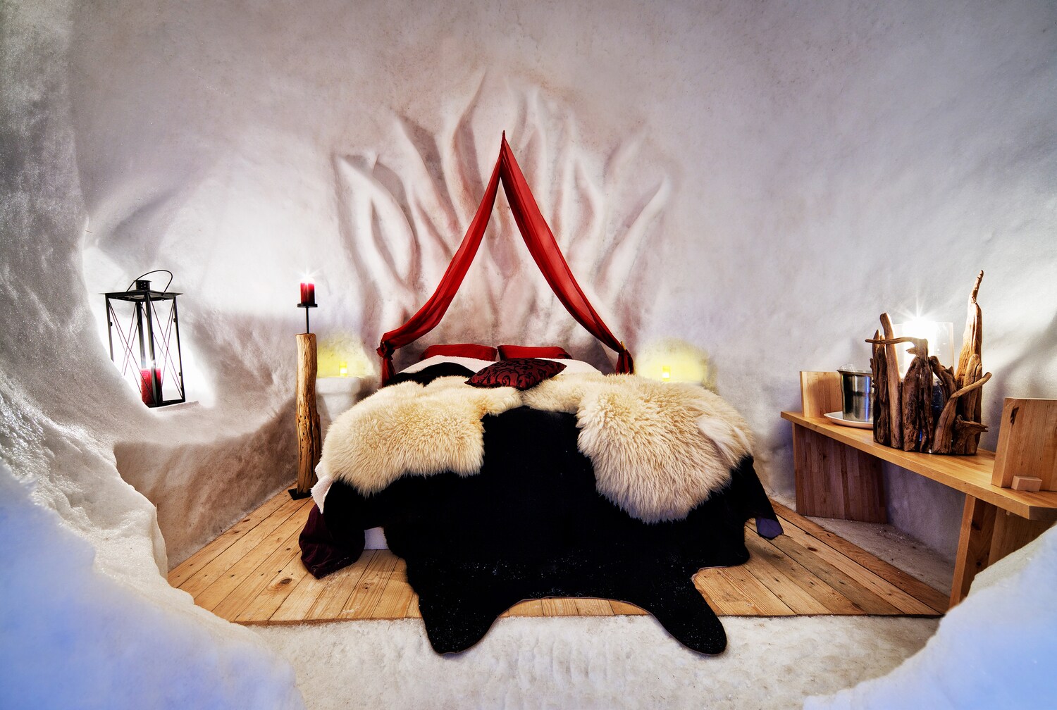 Innenansicht eines Iglu-Hotelzimmers mit Bett, Sideboard und Kerzenbeleuchtung