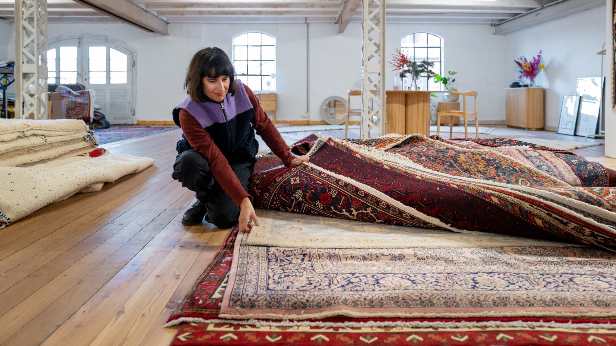 Anna Wahdat durchsucht einen Stapel mit rötlichen Orientteppichen Anna Wahdat durchsucht einen Stapel mit rötlichen Orientteppichen