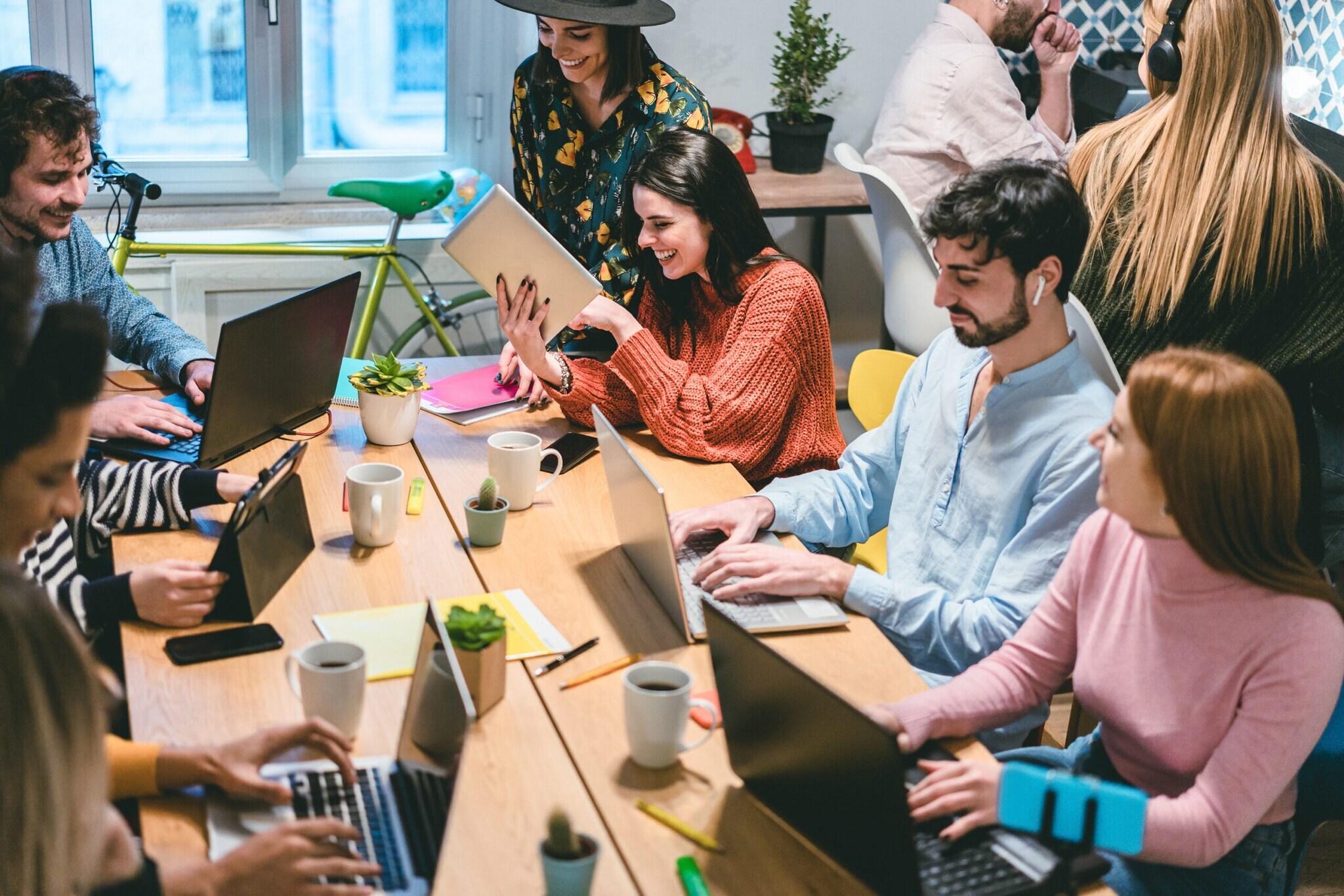 Eine Gruppe junger Leute sitzt zusammen an einem Tisch im Coworking Space und arbeitet mit Laptops