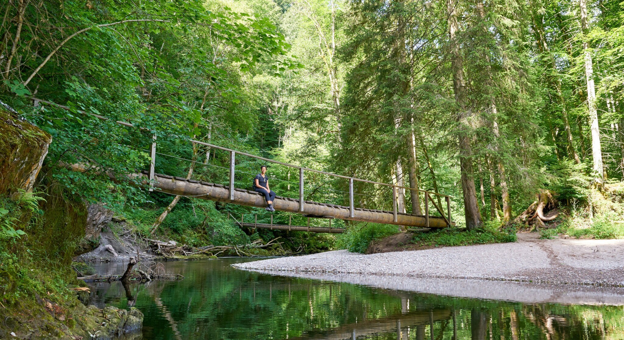 Eine Person sitzt auf einer Holzbrücke über einem Fluss