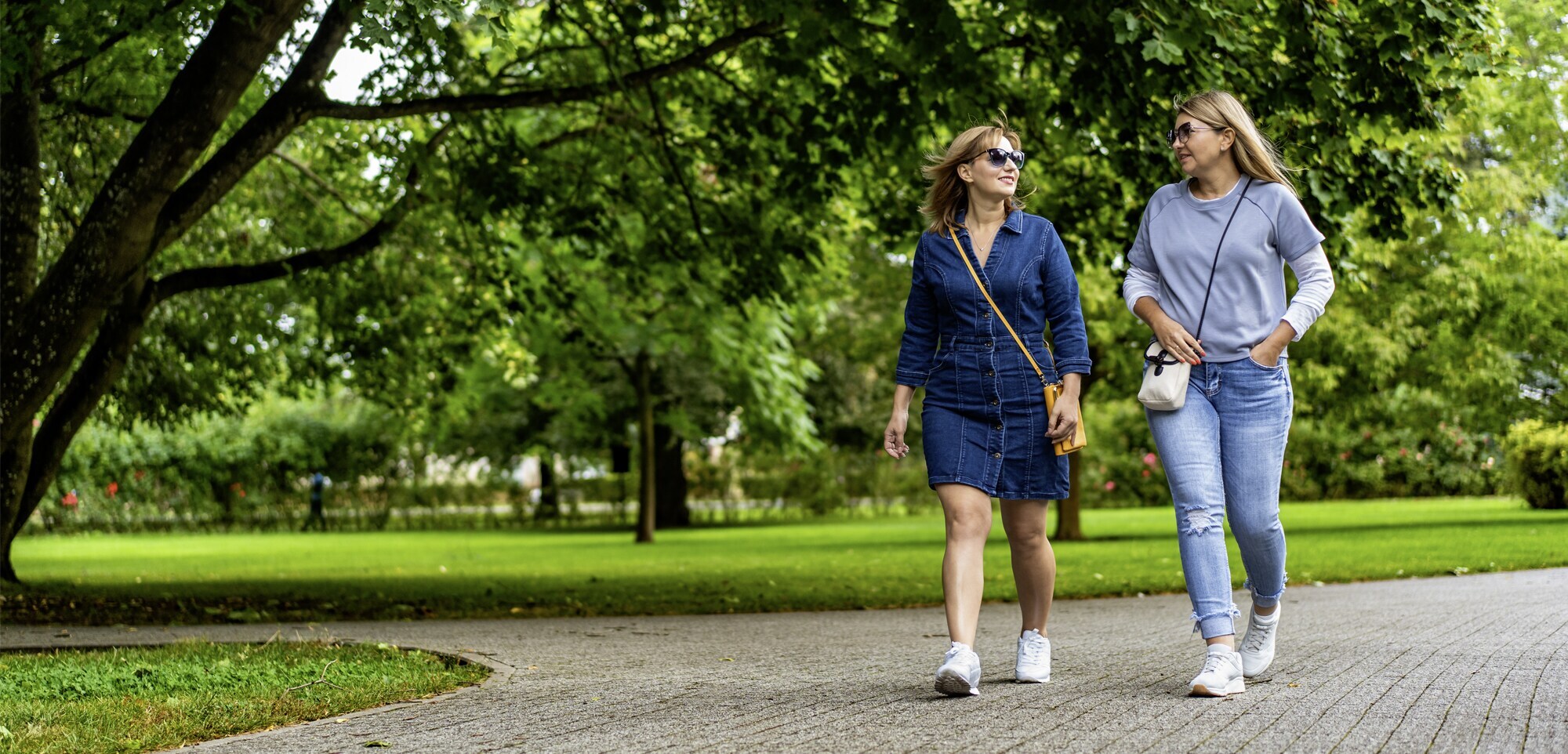 Zwei Frauen spazieren bei frühlingshaftem Wetter durch einen Park.