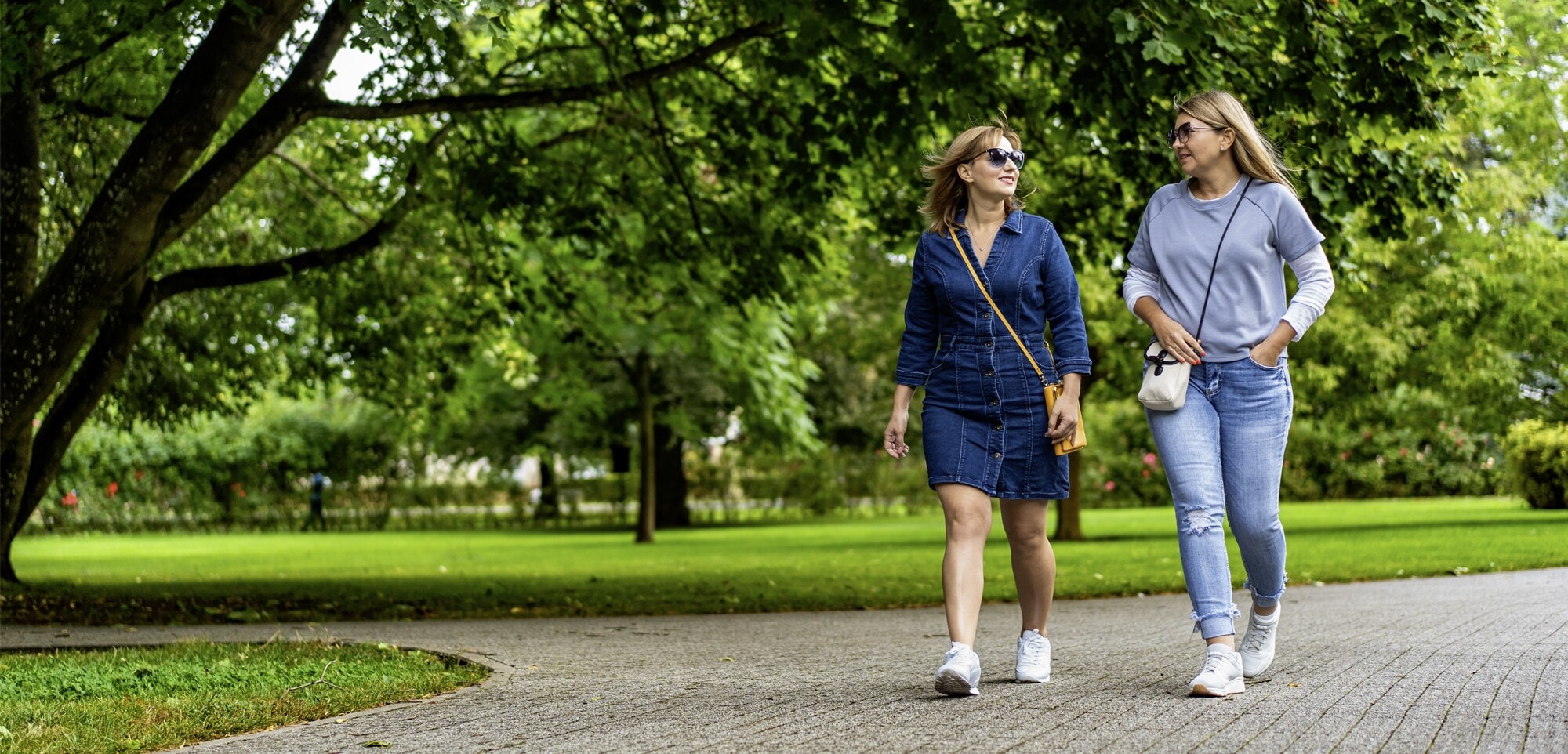Mentale Gesundheit fördern: Mit diesen Strategien klappt es Zwei Frauen spazieren bei frühlingshaftem Wetter durch einen Park.