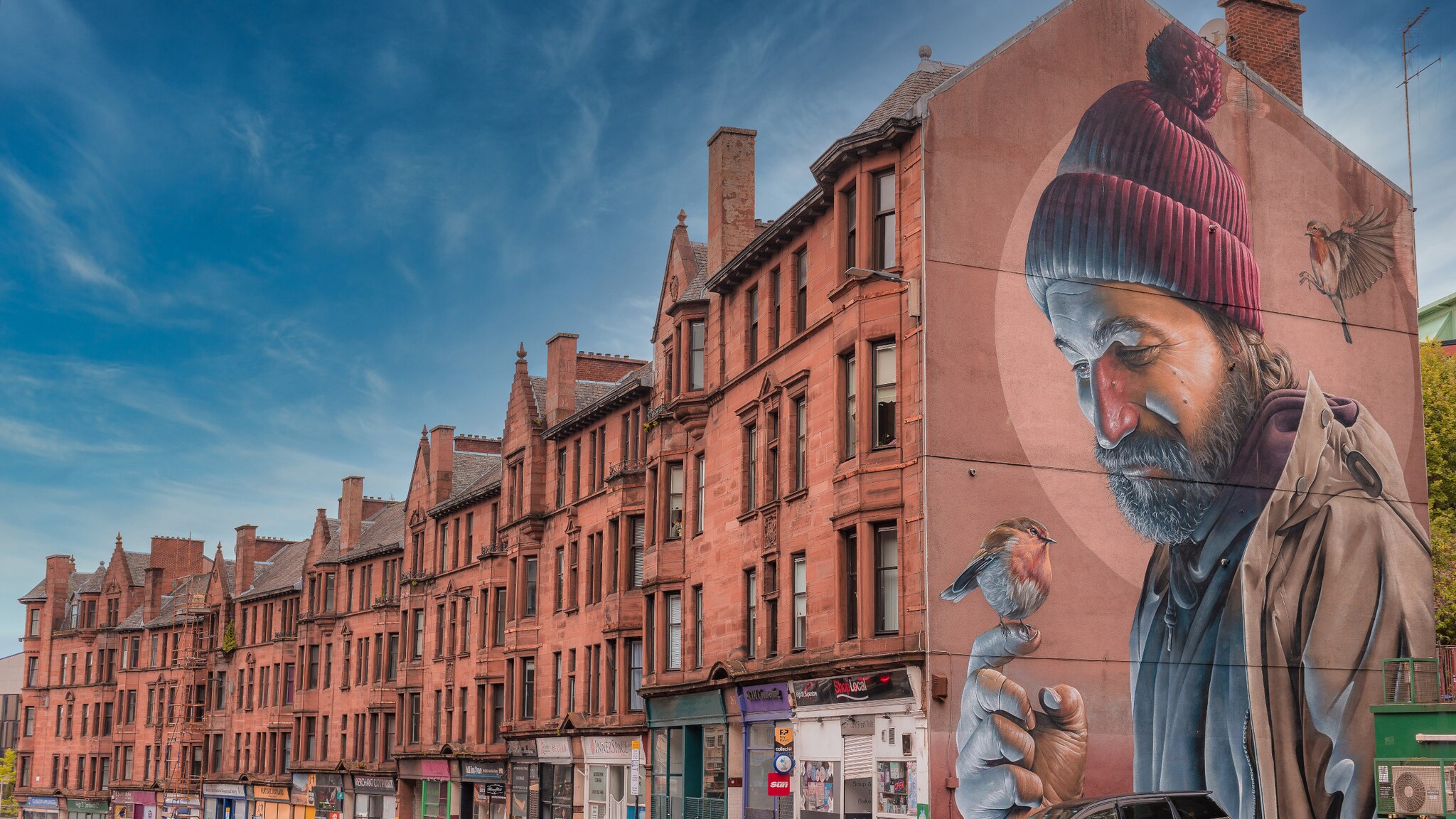 Rotes Backsteingebäude mit Wandgemälde eines Mannes mit roter Mütze und Spatz auf der Hand. Rotes Backsteingebäude mit Wandgemälde eines Mannes mit roter Mütze und Spatz auf der Hand.
