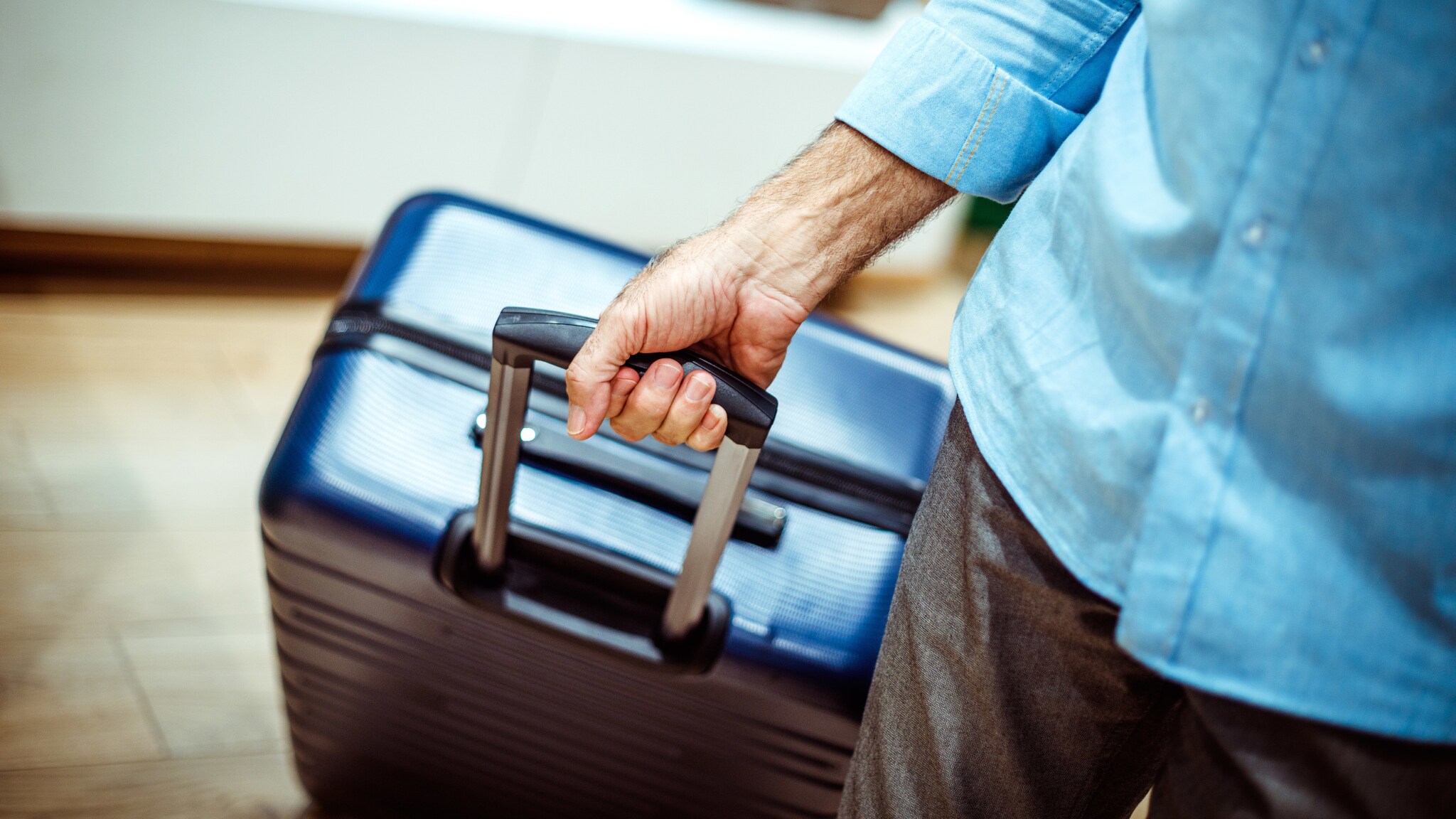 Nahaufnahme einer Hand, die einen blauen Hartschalenkoffer zieht. Nahaufnahme einer Hand, die einen blauen Hartschalenkoffer zieht.