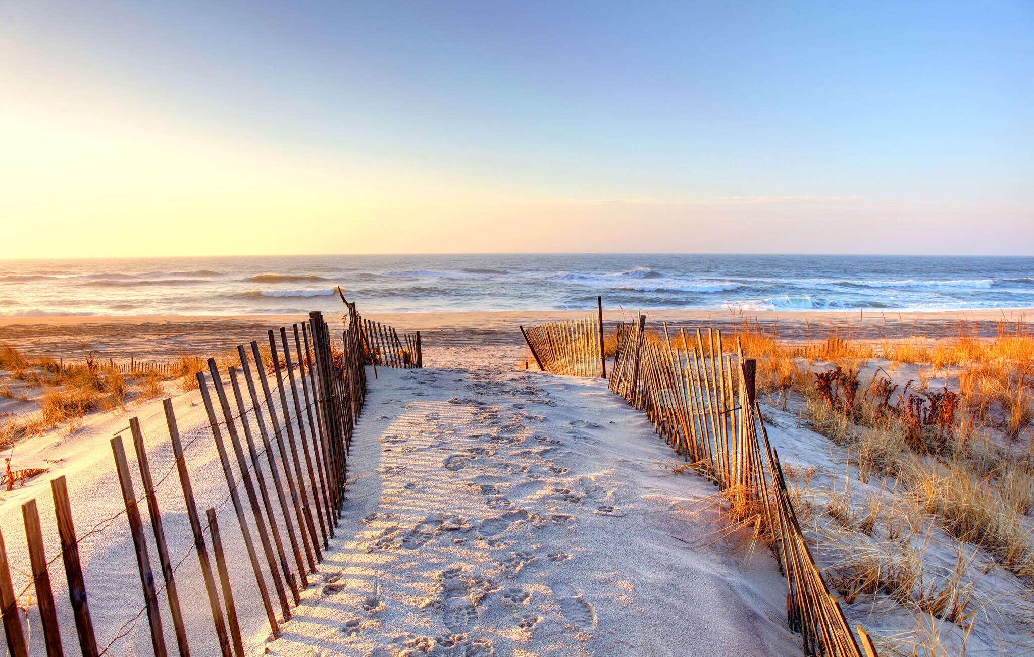 Weg zu einem Sandstrand mit Dünen unter blauem Himmel.