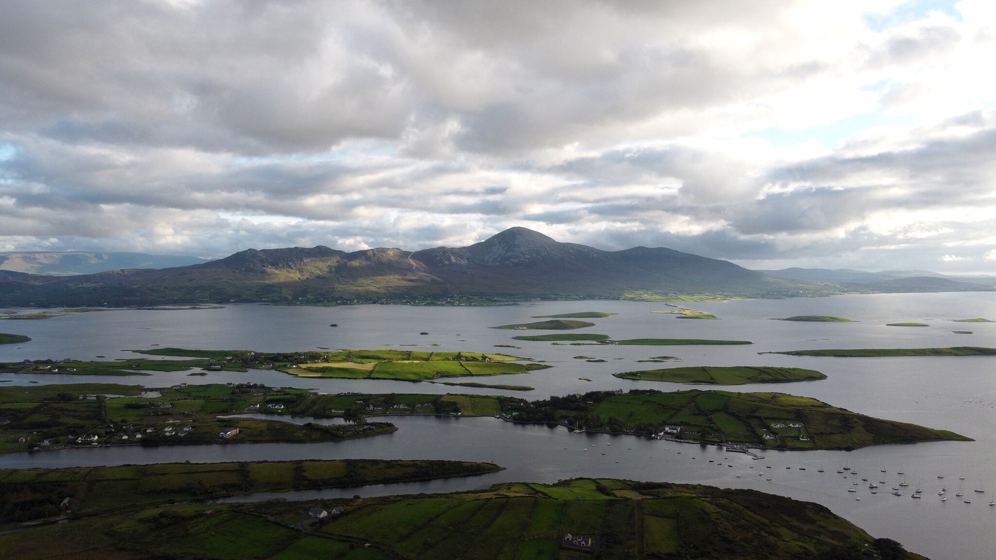 Vor einer Küste liegen etliche kleine, grüne Inseln im Wasser, im Hintergrund ragt ein großer Berg, umgeben von Wolken, empor. Vor einer Küste liegen etliche kleine, grüne Inseln im Wasser, im Hintergrund ragt ein großer Berg, umgeben von Wolken, empor.