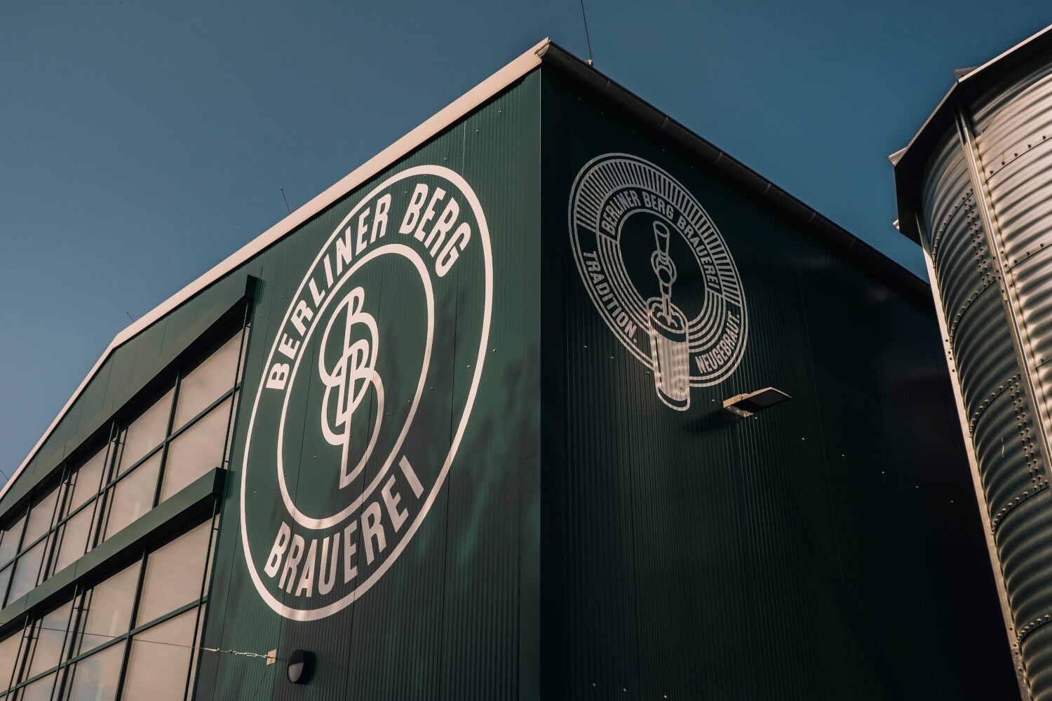Eine dunkelgrüne Fassade eines Fabrikgebäudes vor blauem Himmel