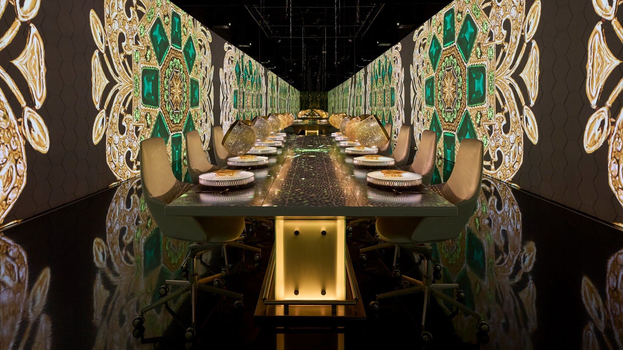 Langer Esstisch mit gedeckten Plätzen in einem Raum mit großen, dekorativen Wandmustern in Grün und Gold
