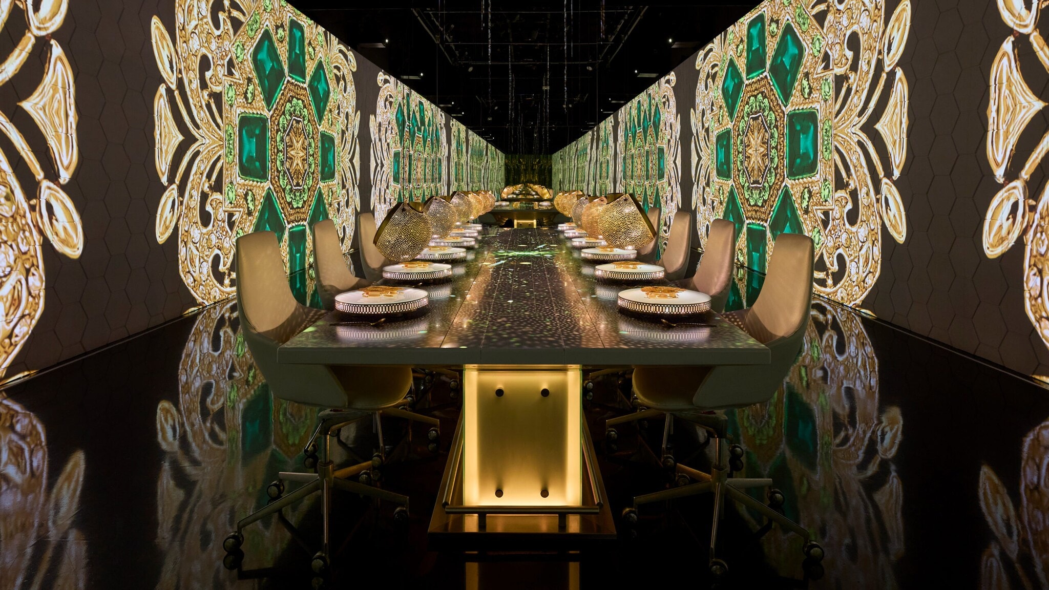 Langer Esstisch mit gedeckten Plätzen in einem Raum mit großen, dekorativen Wandmustern in Grün und Gold Langer Esstisch mit gedeckten Plätzen in einem Raum mit großen, dekorativen Wandmustern in Grün und Gold