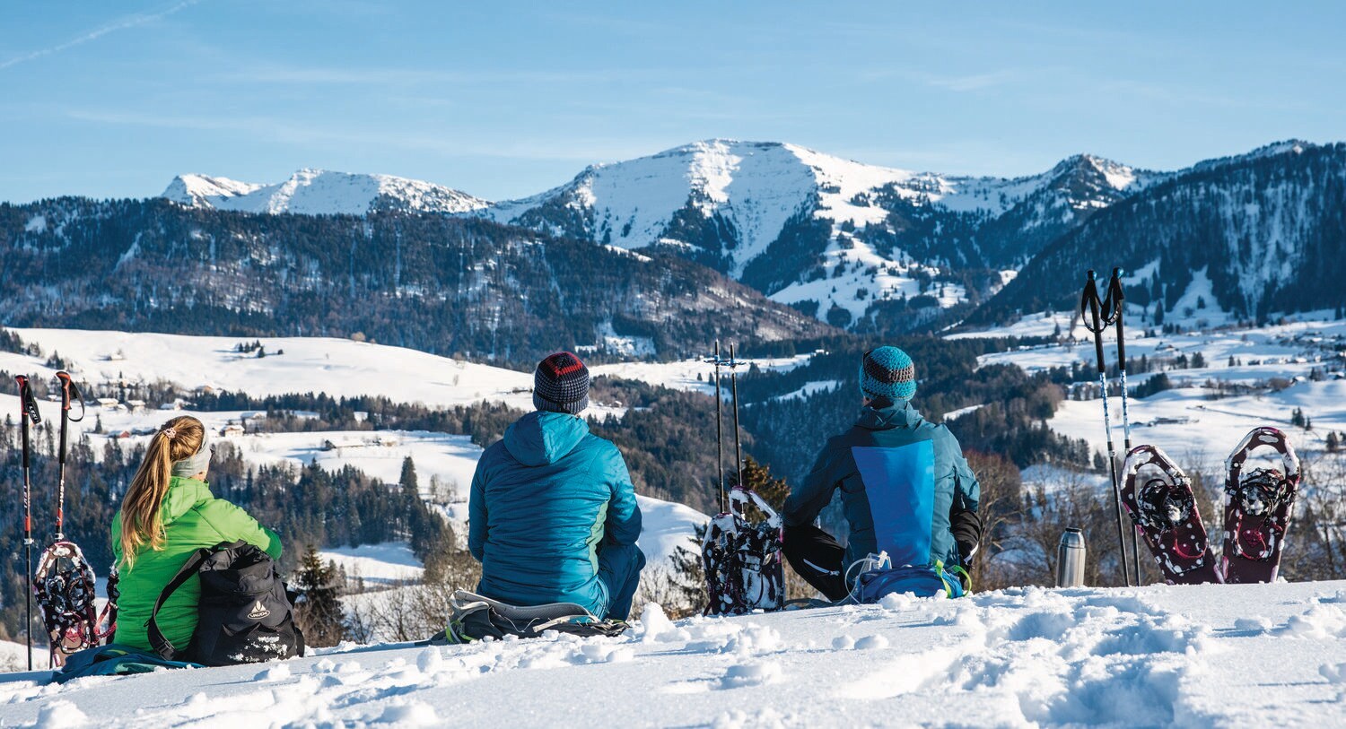Drei Menschen in Winterkleidung sitzen im Schnee und blicken in die Ferne