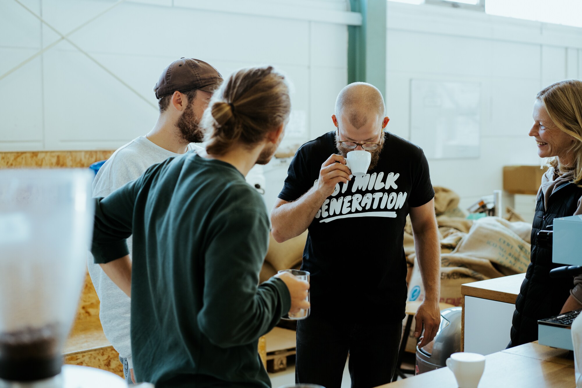 Ein Mann riecht im Kreise drei weiterer Personen an einer Kaffeetasse in einem Geschäft Ein Mann riecht im Kreise drei weiterer Personen an einer Kaffeetasse in einem Geschäft
