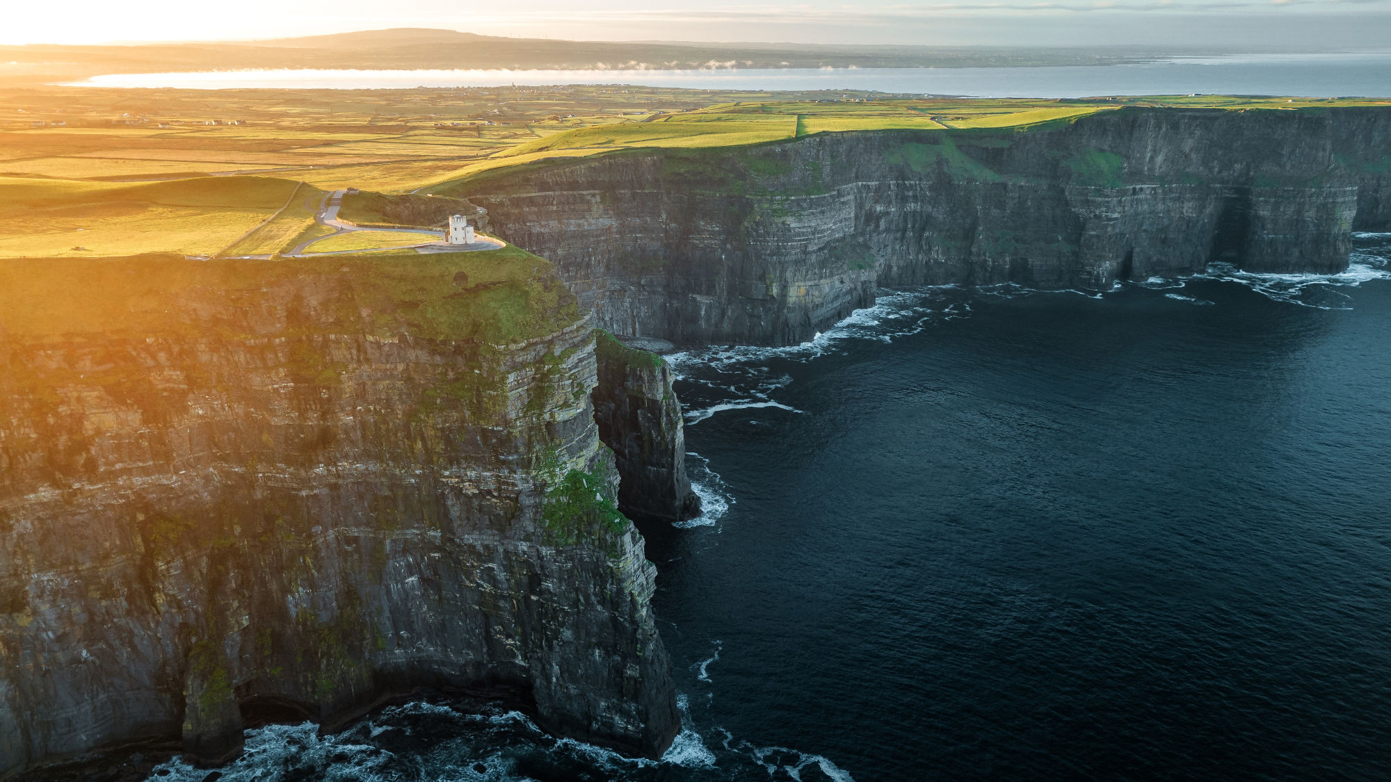 Die Klippen von Moher in County Clare, steile Felsen, die ins Meer ragen, mit grünem Gras und Wiesen im Hintergrund, bei Sonnenuntergang. Die Klippen von Moher in County Clare, steile Felsen, die ins Meer ragen, mit grünem Gras und Wiesen im Hintergrund, bei Sonnenuntergang.