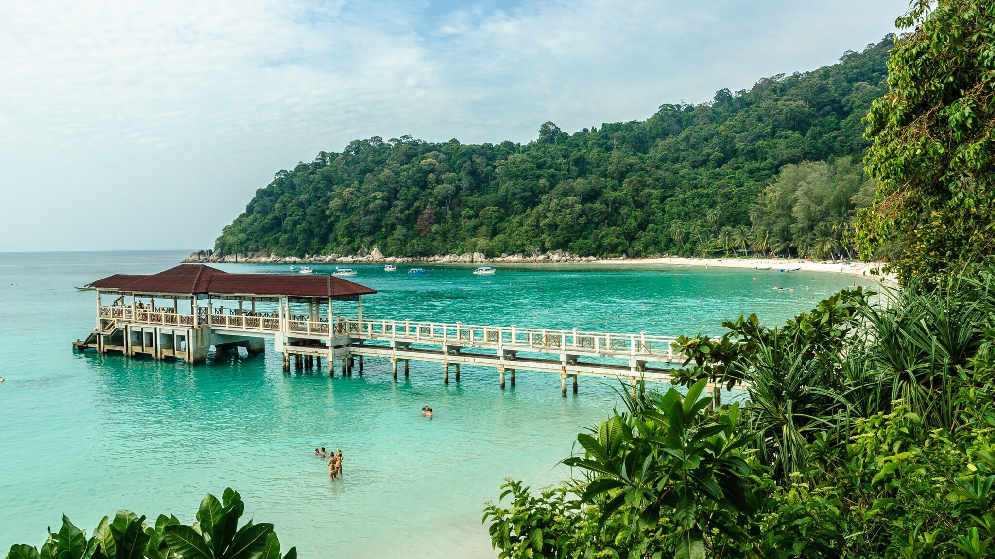Holzsteg mit überdachtem Bereich ragt in türkisfarbenes Meer an einem tropischen Strand mit dichtem Dschungel im Hintergrund. Holzsteg mit überdachtem Bereich ragt in türkisfarbenes Meer an einem tropischen Strand mit dichtem Dschungel im Hintergrund.