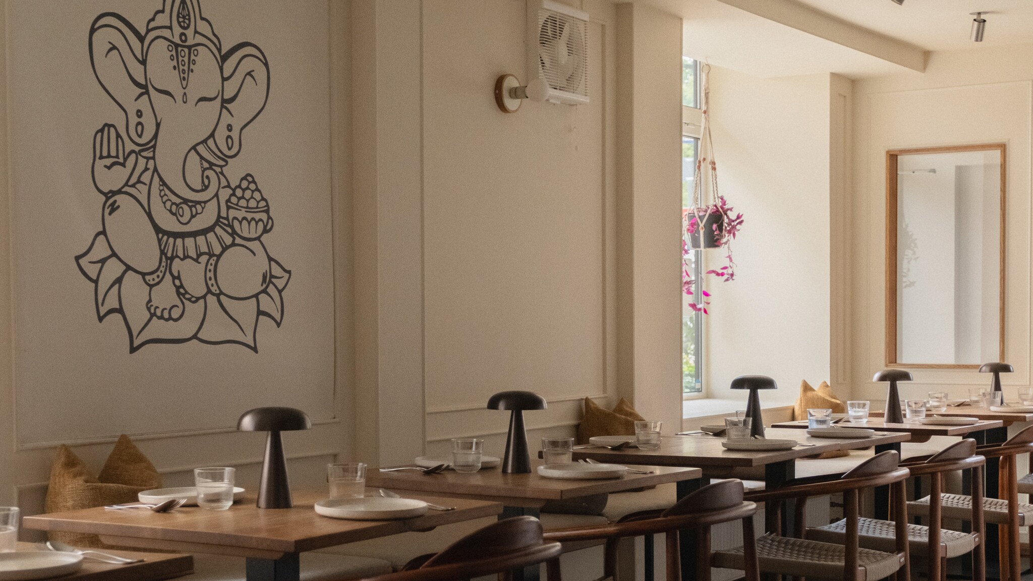 in Restaurant mit Holztischen und Stühlen. An der Wand ist eine große, schwarze Darstellung von Ganesha. Es gibt Fenster mit natürlichem Licht.