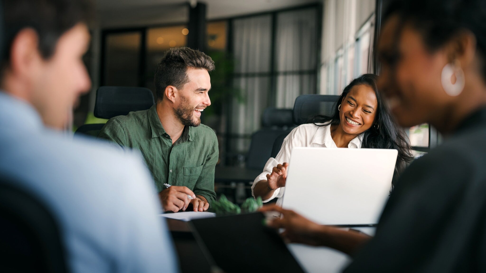 Vier Personen sitzen lächelnd beisammen an einem Arbeitstisch. Vier Personen sitzen lächelnd beisammen an einem Arbeitstisch.