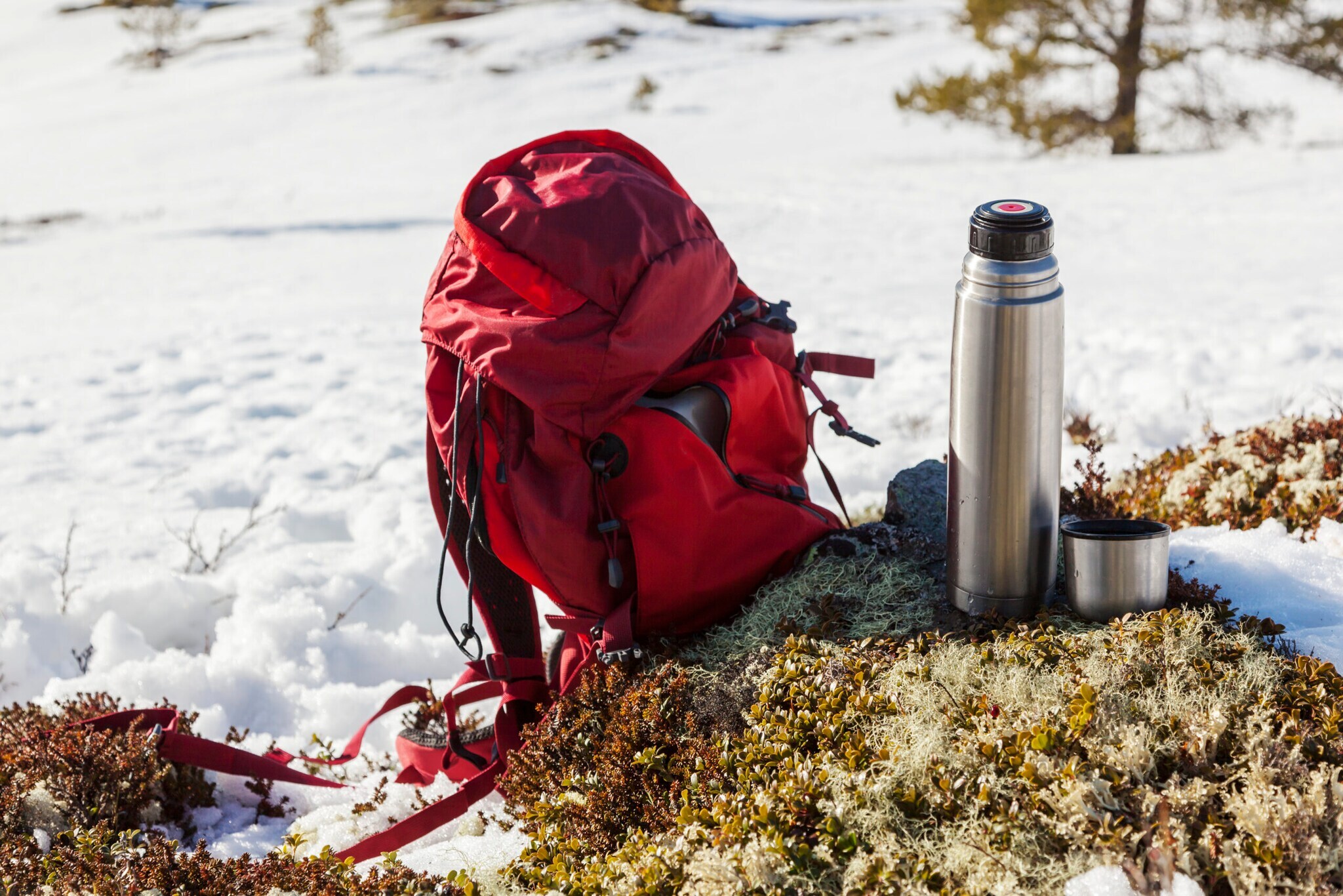 Ein Rucksack und eine Thermoskanne, im Hintergrund Schnee