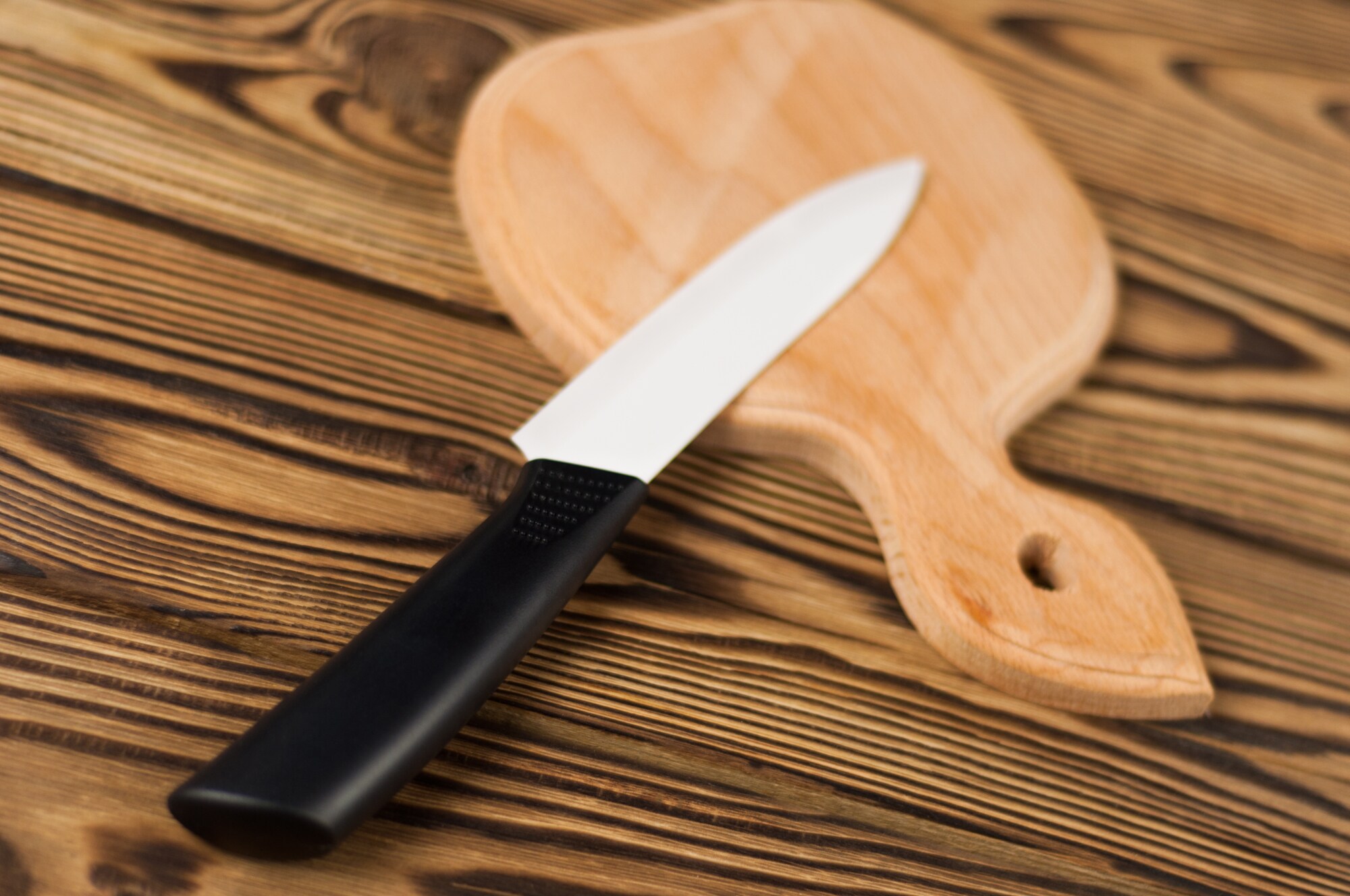 Keramikmesser mit schwarzem Griff und Holzbrett auf Holztisch