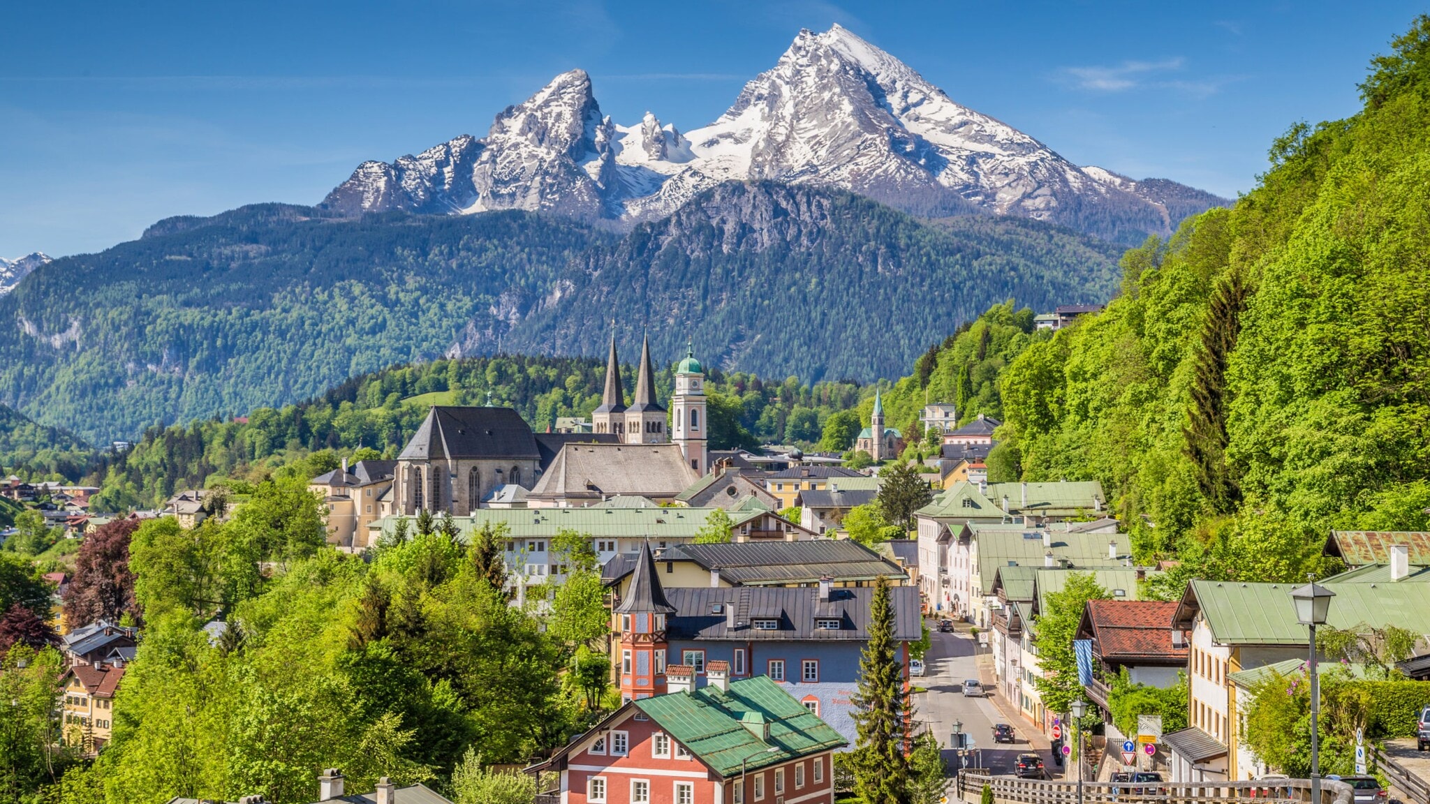 Blick auf eine Stadt mit historischen Gebäuden und einer Kirche vor bewaldeten Hügeln und schneebedeckten Bergen im Hintergrund. Blick auf eine Stadt mit historischen Gebäuden und einer Kirche vor bewaldeten Hügeln und schneebedeckten Bergen im Hintergrund.