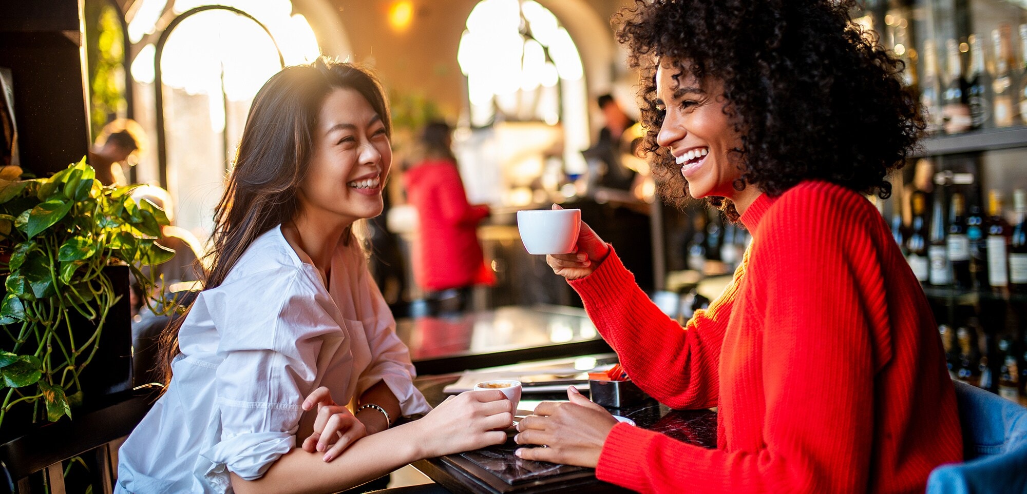 Zwei Geschäftsfrauen unterschiedlicher Nationalitäten sitzen in einer Bar und trinken Kaffee.
