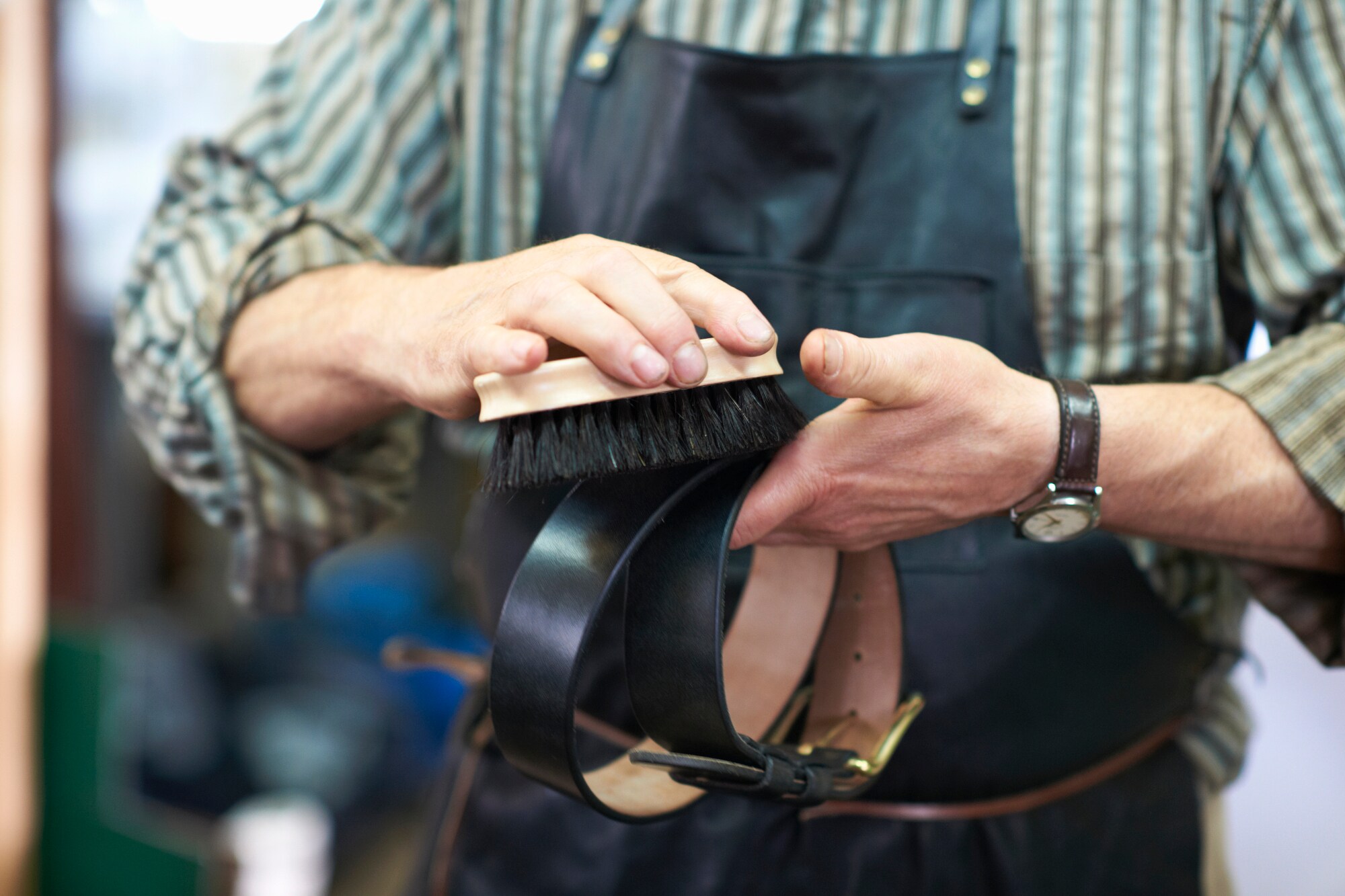 Ein Mann mit Schürze poliert einen schwarzen Ledergürtel mit einer Bürste