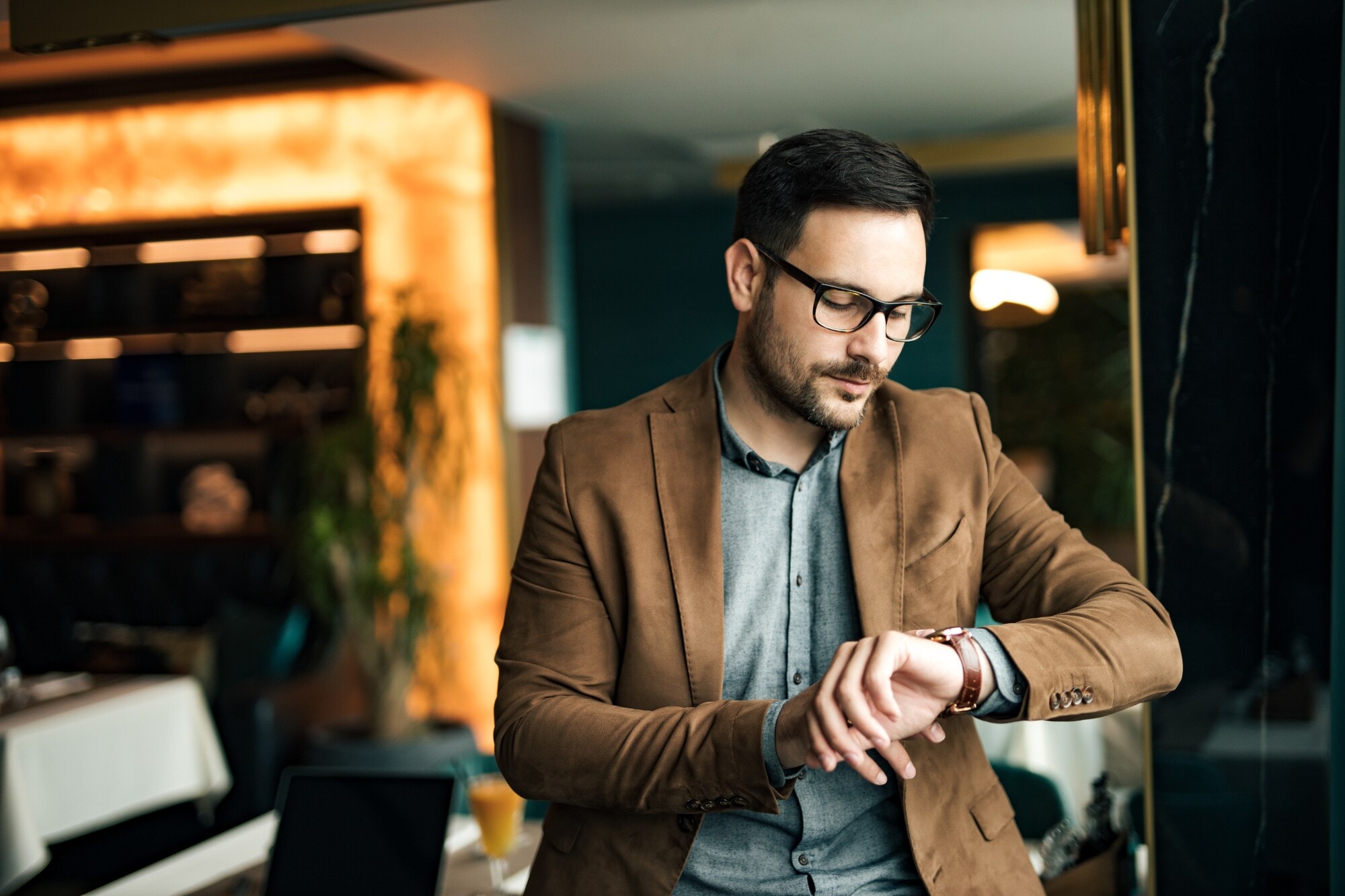 Ein Mann im Jacket, mit Brille und Bart schaut auf seine Armbanduhr Ein Mann im Jacket, mit Brille und Bart schaut auf seine Armbanduhr