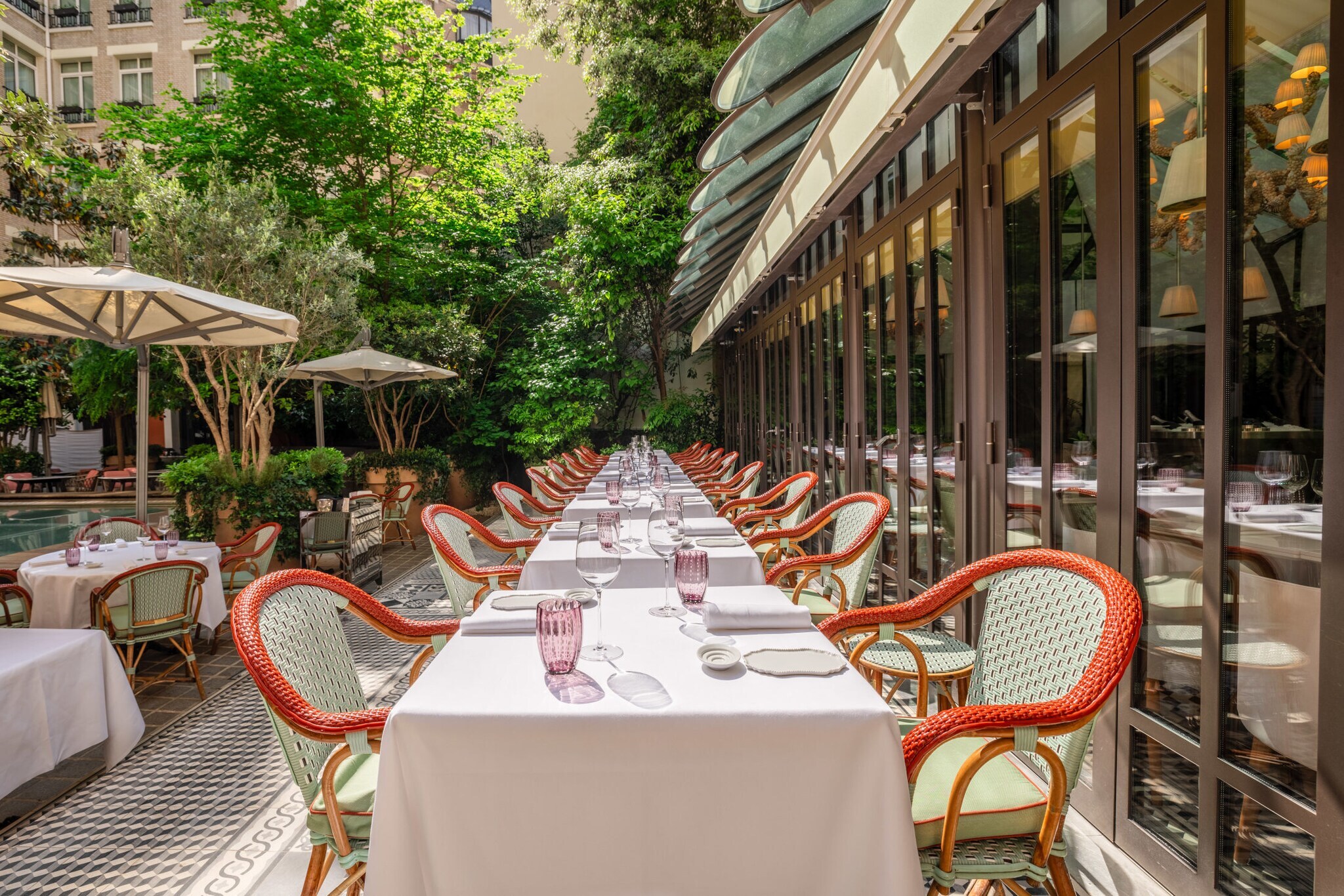 Begrünter Innenhof eines eleganten Restaurants mit gedeckten Tischen und Sonnenschirmen.