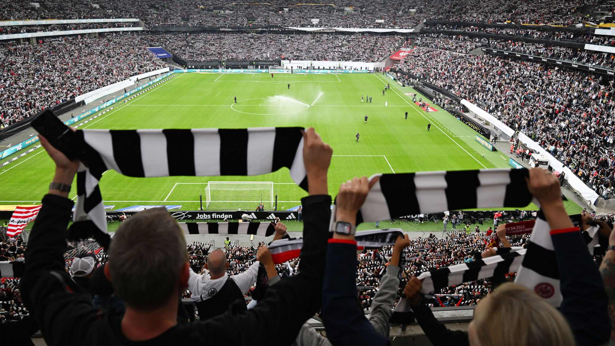 Rückansicht von Personen, die schwarz-weiß gestreifte Schals hochhalten in einem gefüllten Fußballstadion. Rückansicht von Personen, die schwarz-weiß gestreifte Schals hochhalten in einem gefüllten Fußballstadion.