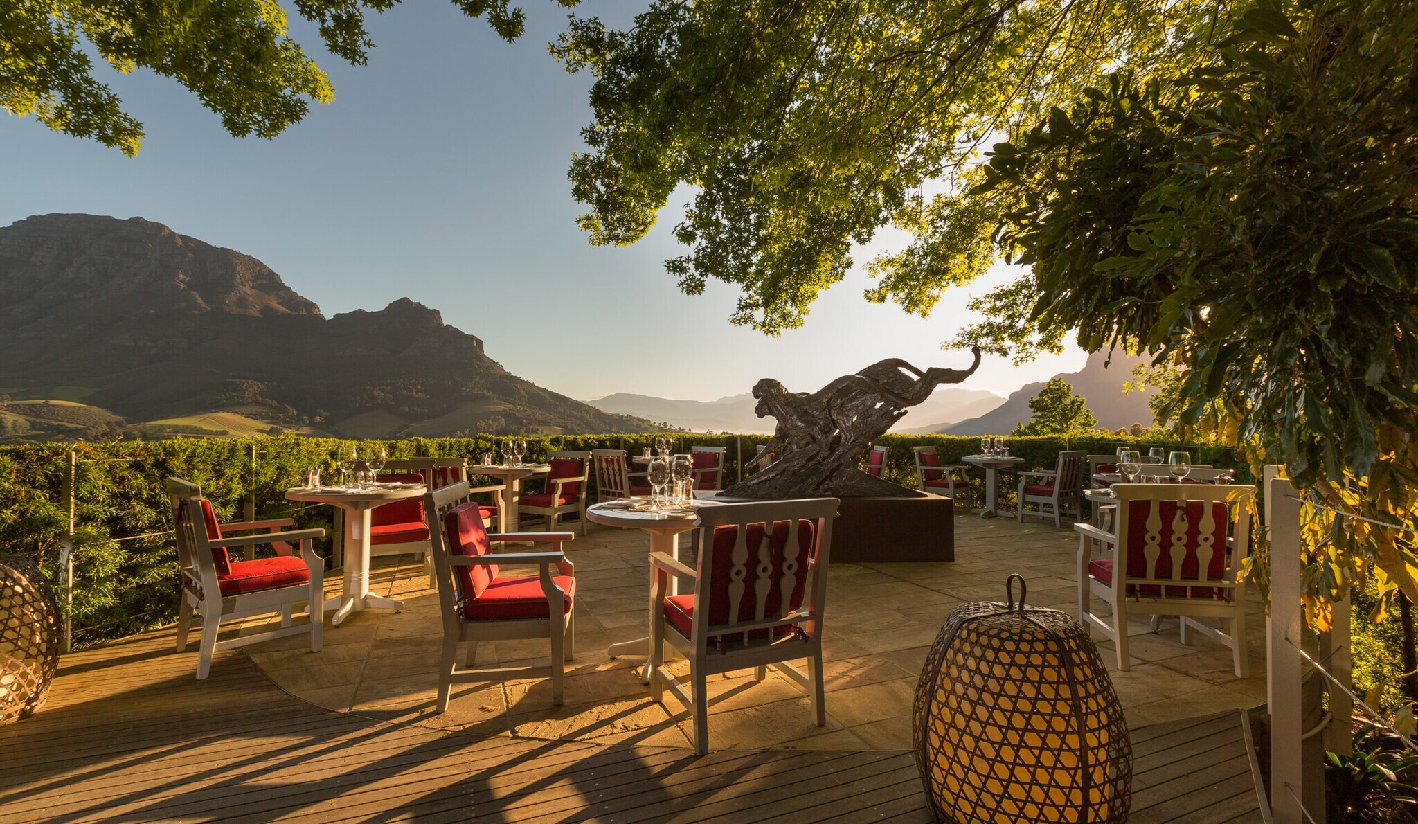 Elegante Terrasse mit weißen Tischen und roten Polsterstühlen mit Blick auf eine gebirgige Landschaft in der Abendsonne