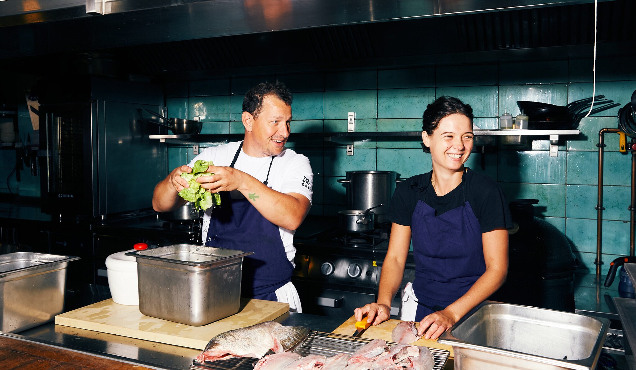 Koch und Köchin bereiten Salat und Fisch in der Restaurantküche vor.