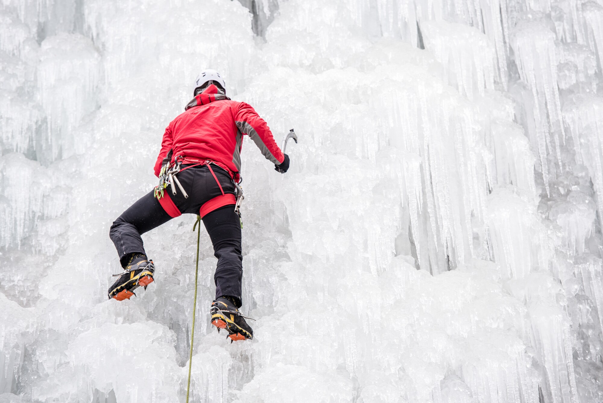 Eiskletterer hängt an vereister Felswand mit Eiszapfen