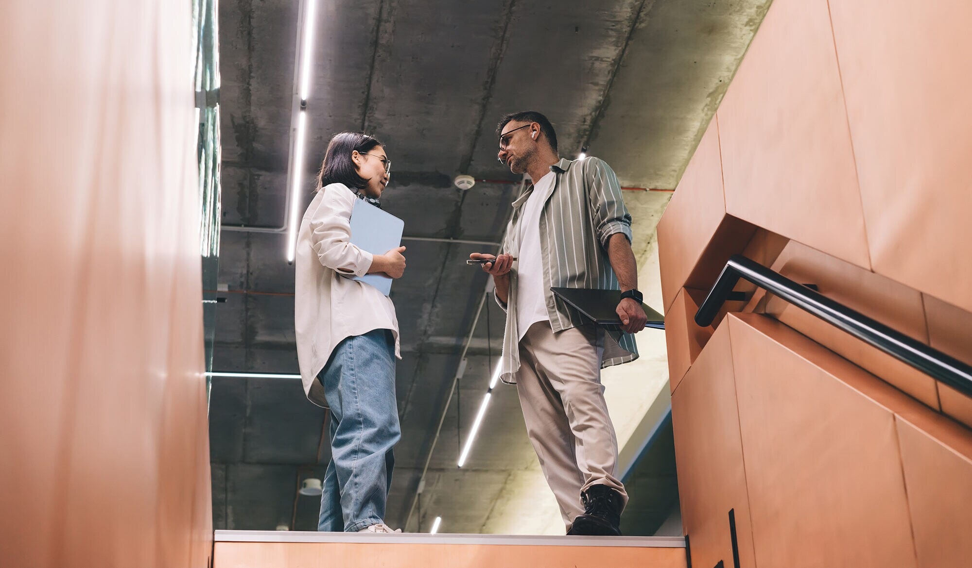 Soft Skills, die zählen: Stärke dein Business & dein Team Zwei Kolleg:innen begegnen sich auf der Treppe und sprechen miteinander.