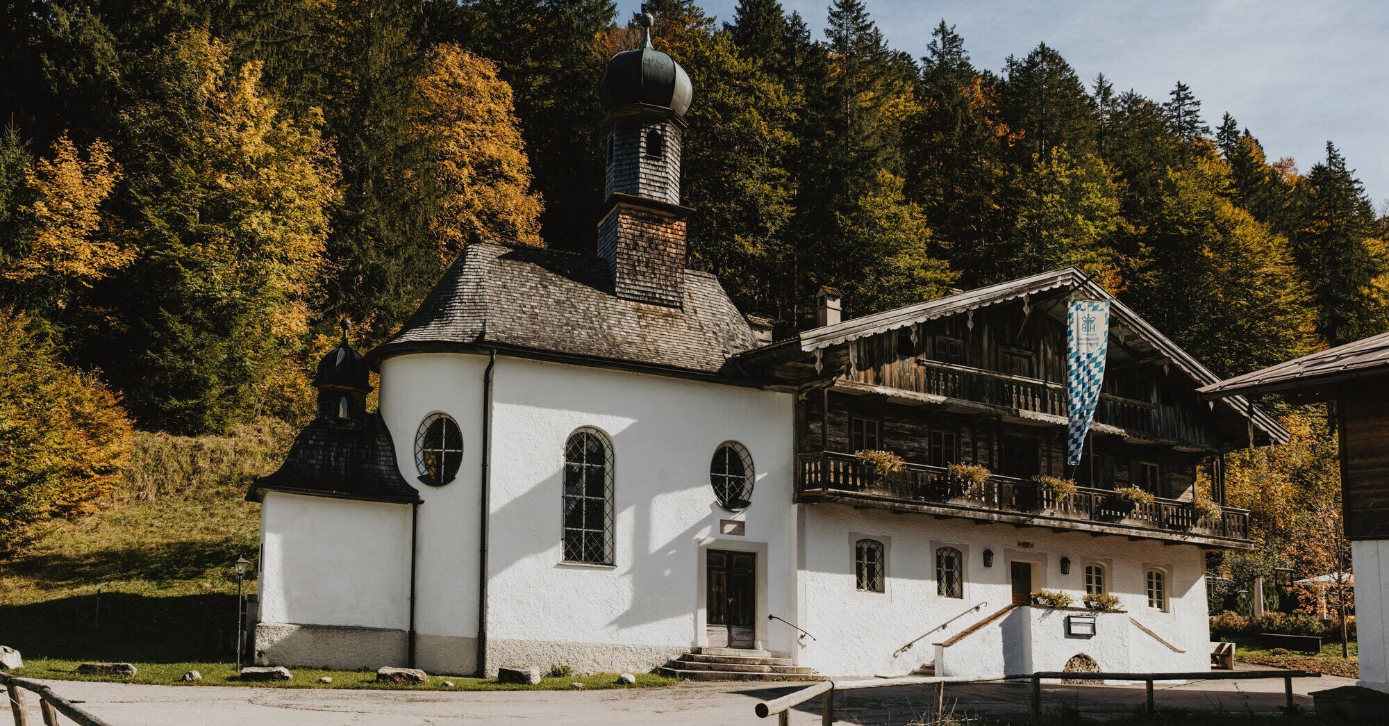 Traditionelles, bayerisches Gasthaus mit Kapelle vor einem Waldgebiet.