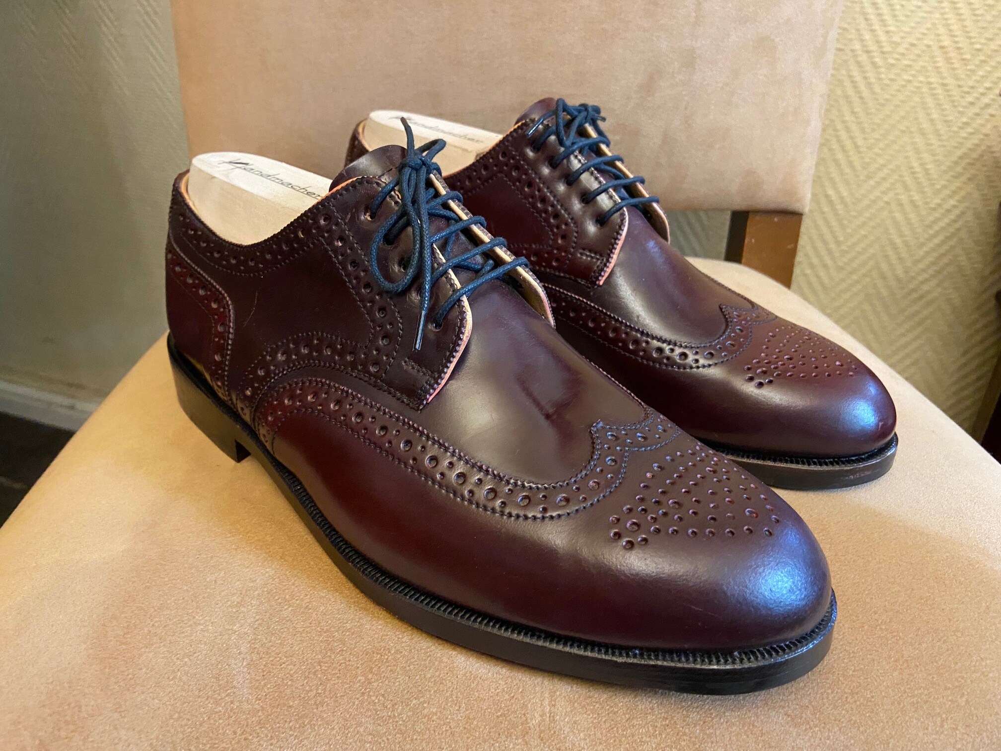 Braune Lederschuhe mit gestanzten Verzierungen auf einem Polsterstuhl