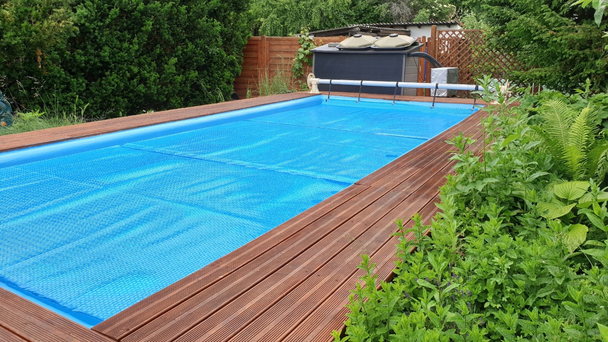 In einem Garten ist ein Pool mit einer blauen Plane bedeckt. In einem Garten ist ein Pool mit einer blauen Plane bedeckt.