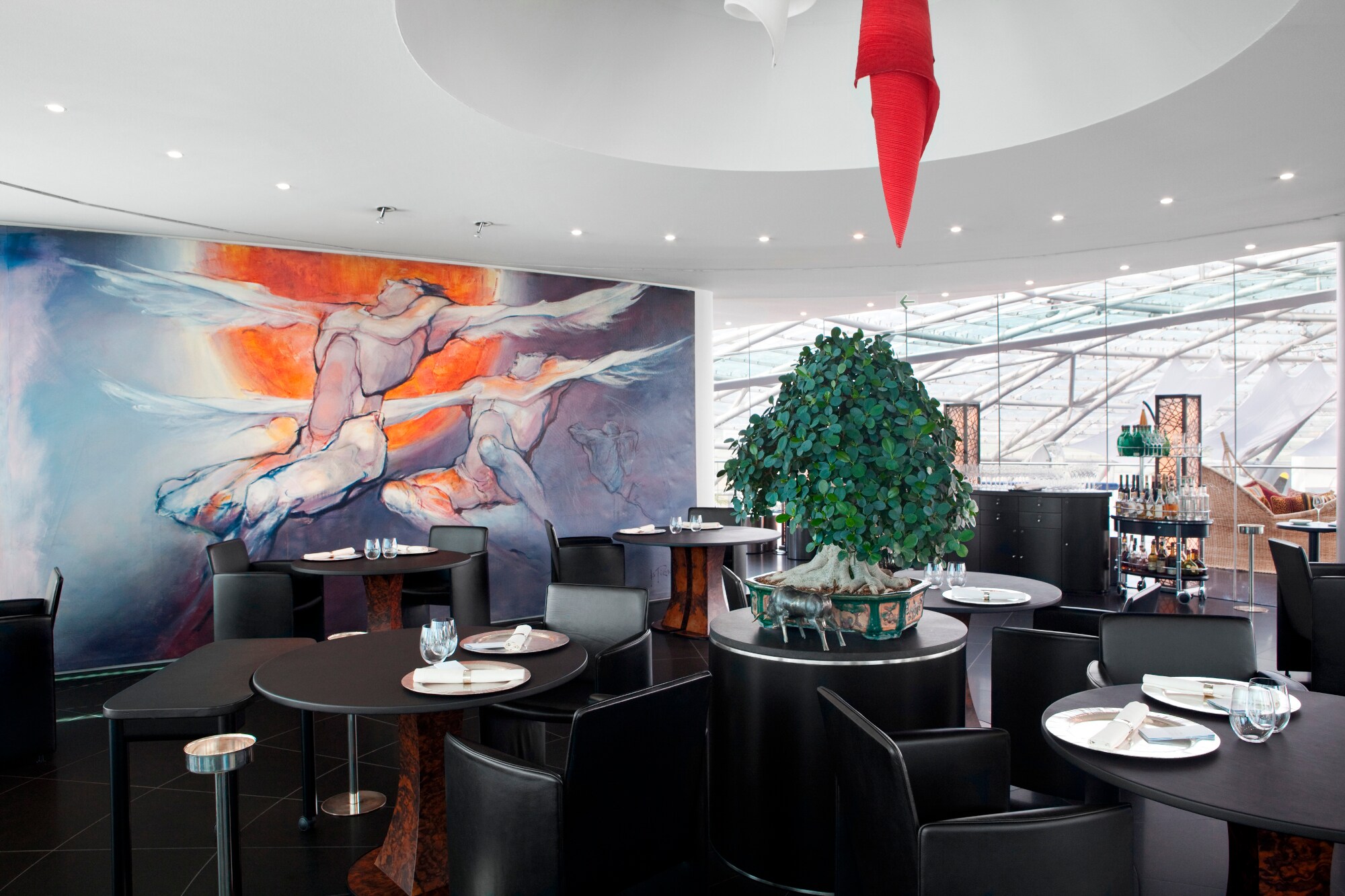 Mehrere dunkle, eingedeckte Tische im Restaurant Ikarus, im Hintergrund ein großes Ikarusgemälde, rechts die Glaswand des Hanger-7.