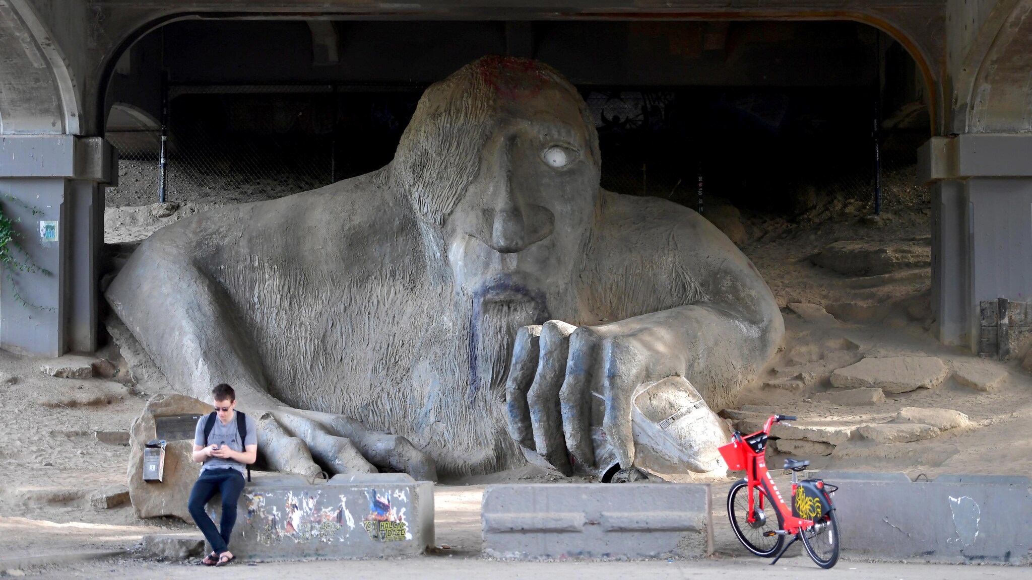 Skulptur eines überdimensionierten Trolls unter einer Brücke.