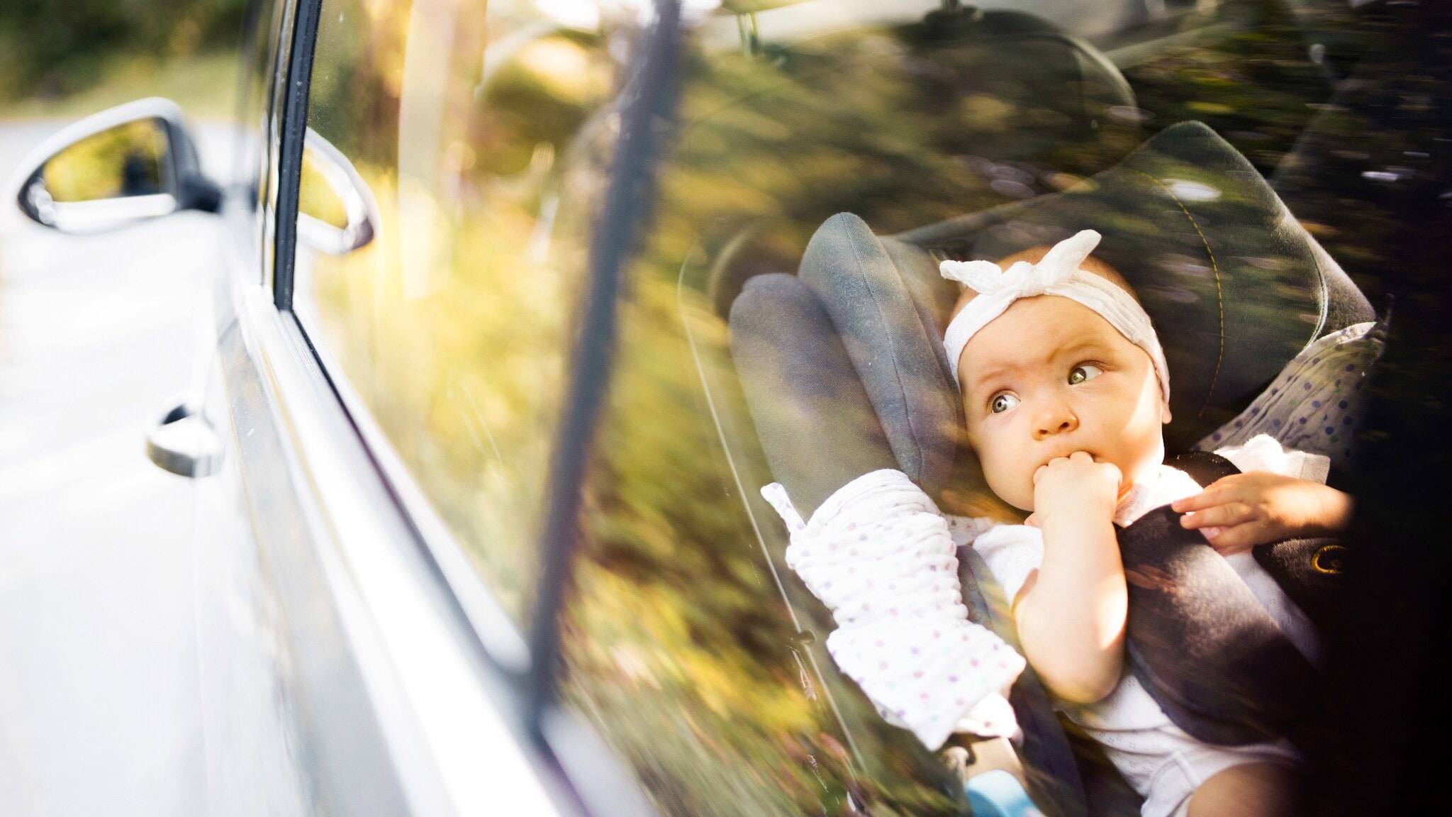 Kind sitzt auf dem Rücksitz eines Autos, hält ein Taschentuch und trägt eine weiße Bluse mit schwarzen Punkten. Kind sitzt auf dem Rücksitz eines Autos, hält ein Taschentuch und trägt eine weiße Bluse mit schwarzen Punkten.