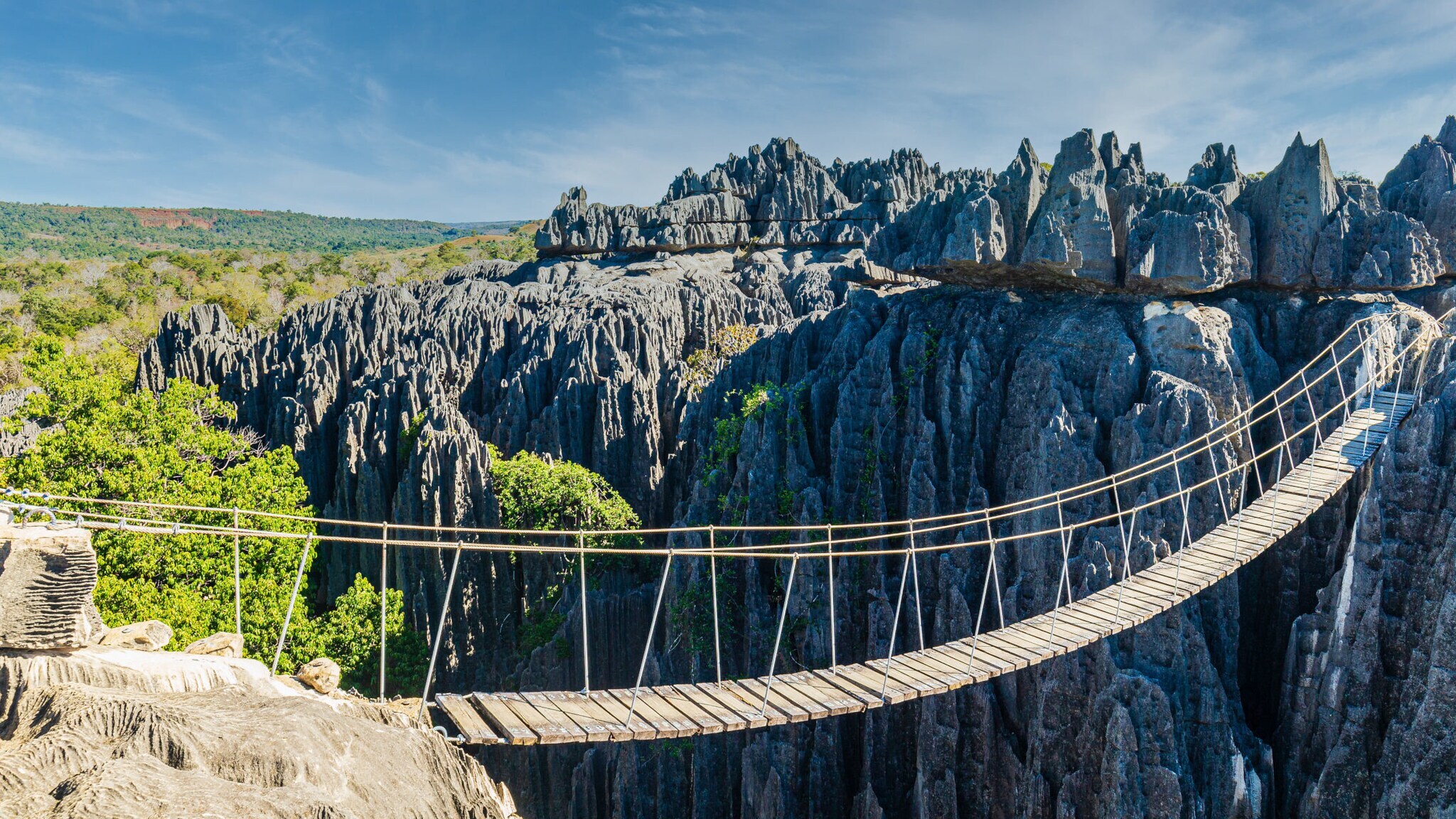 Eine Schlucht mit Hängebrücke, die zu einer Felsformation im Gebiet Tsingy de Bemaraha auf Madagaskar führt.