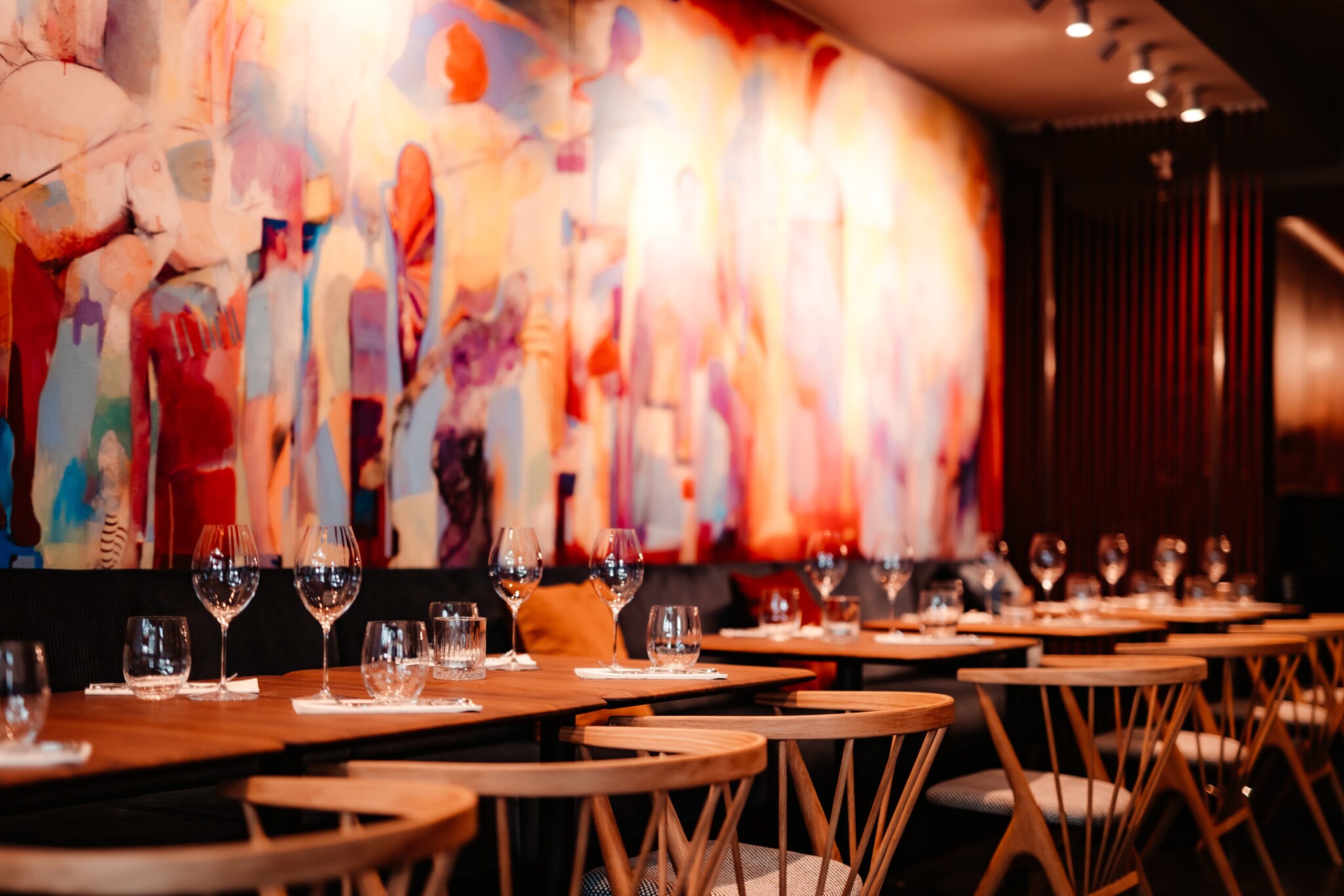 Mehrere eingedeckte Holztische vor einem bunten, großflächigem Wandbild.