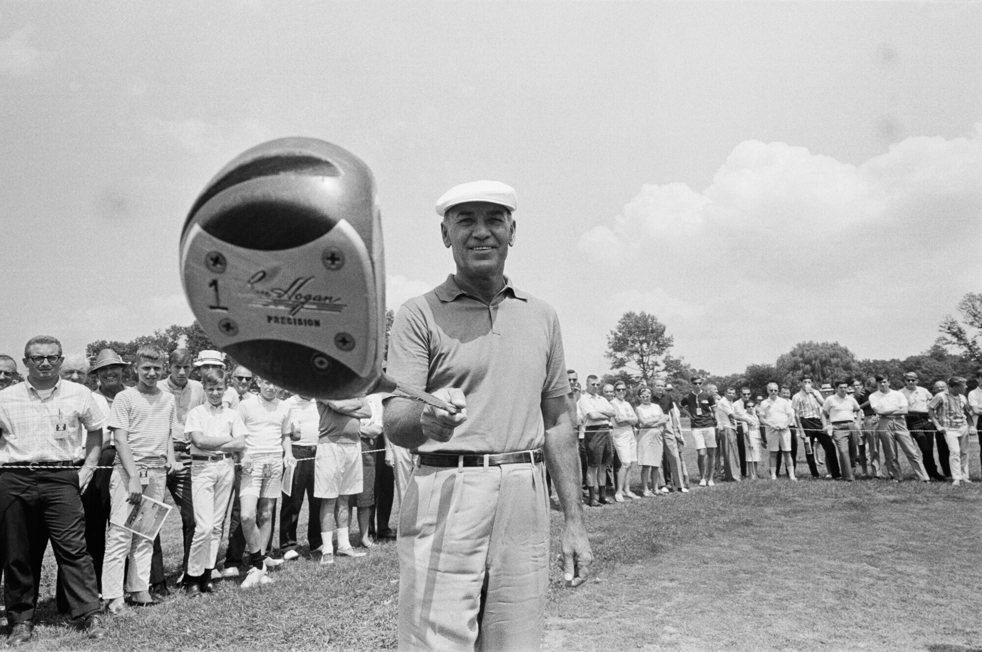 Ben Hogan hält seinen Schläger auf dem Golfplatz in die Kamera, im Hintergrund steht Publikum Ben Hogan hält seinen Schläger auf dem Golfplatz in die Kamera, im Hintergrund steht Publikum