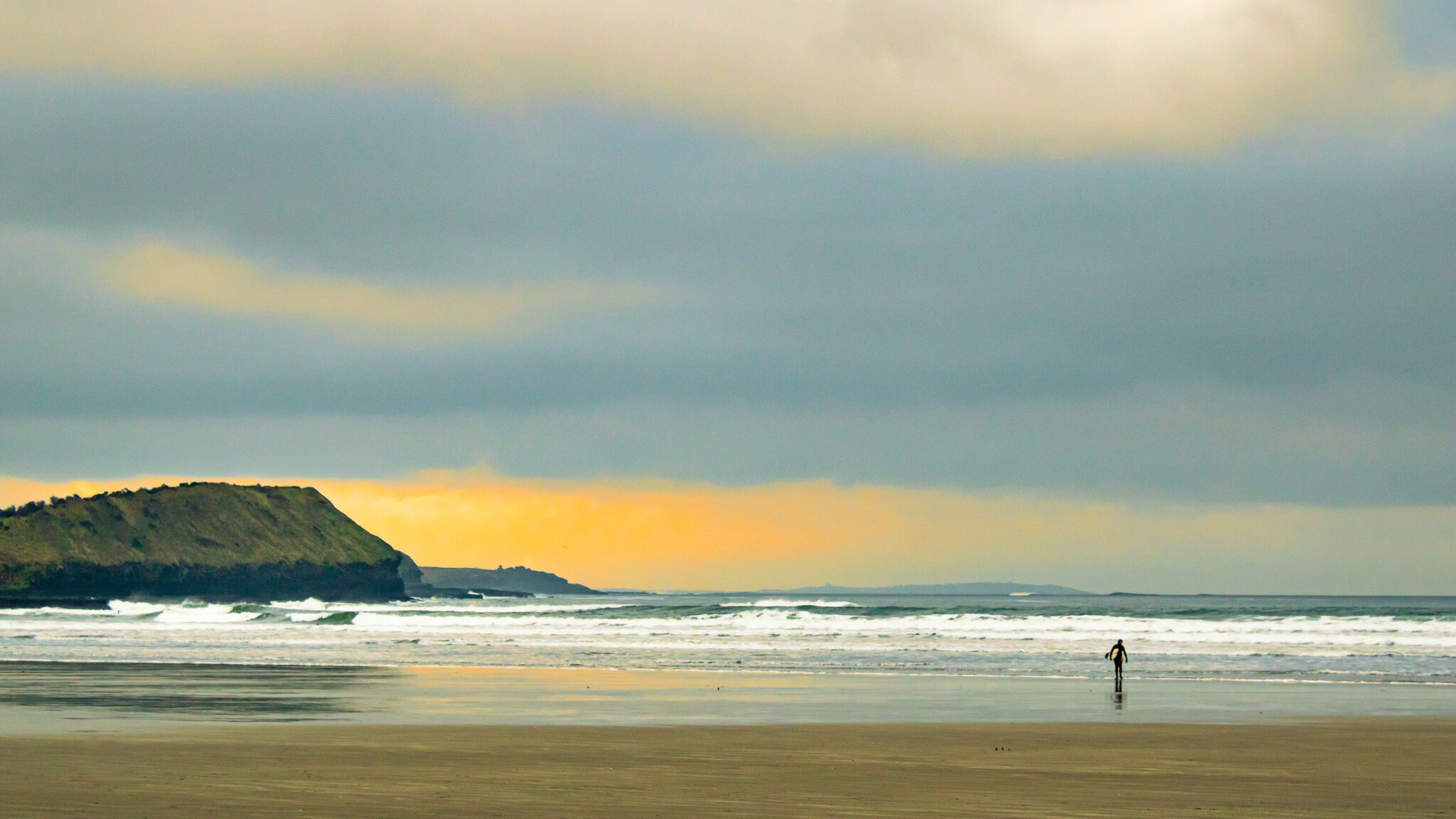 Eine Person steht im flachen Wasser am Strand, während die Wellen sanft an den Ufer schlagen. Im Hintergrund ist eine bewaldete Küstenlinie und ein bewölkter Himmel zu sehen. Eine Person steht im flachen Wasser am Strand, während die Wellen sanft an den Ufer schlagen. Im Hintergrund ist eine bewaldete Küstenlinie und ein bewölkter Himmel zu sehen.