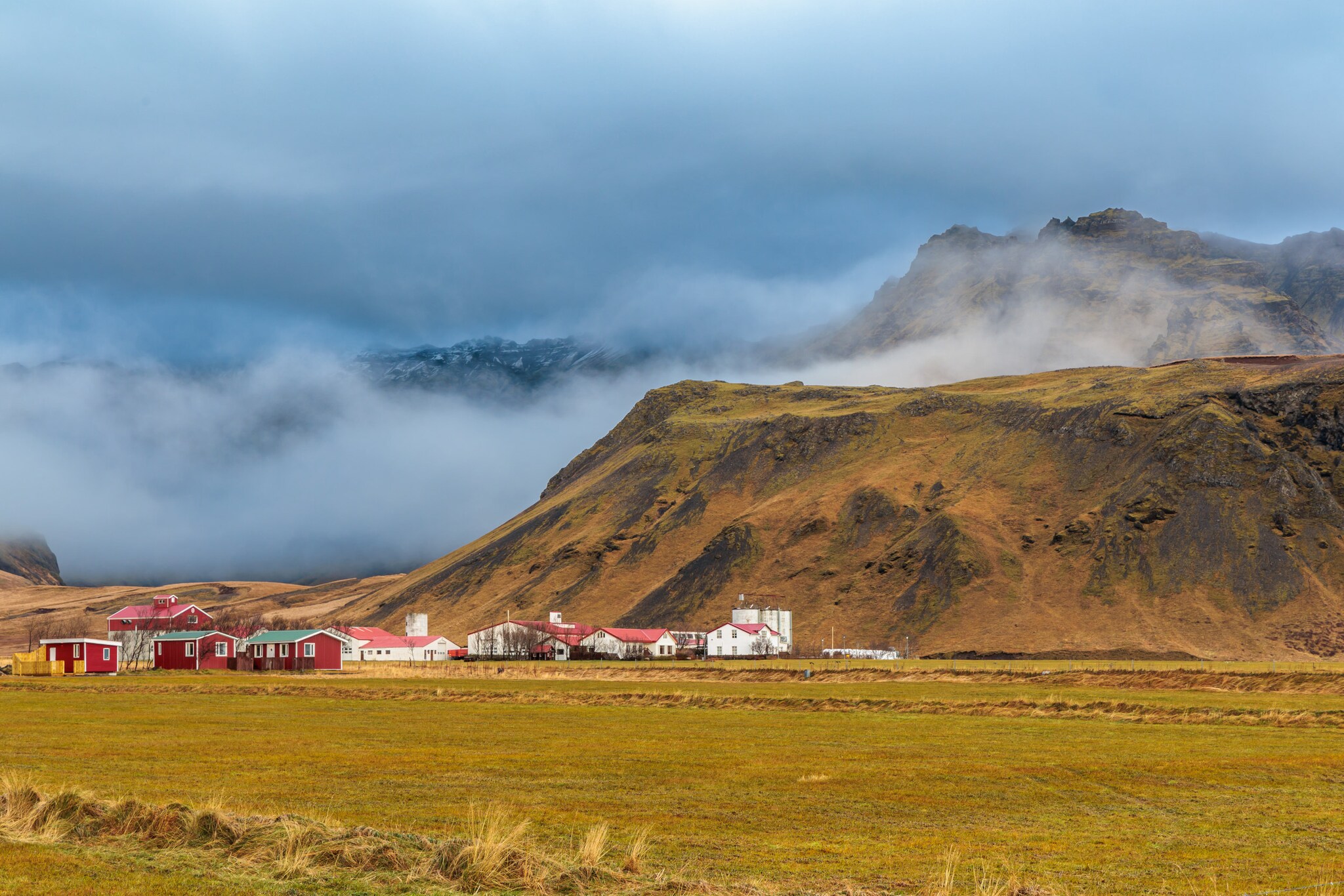 Faszinierende und neblige Herbstlandschaft rund um den Vulkan Eyjafjallajökull mit einer kleinen Siedlung im Vordergrund. Faszinierende und neblige Herbstlandschaft rund um den Vulkan Eyjafjallajökull mit einer kleinen Siedlung im Vordergrund.