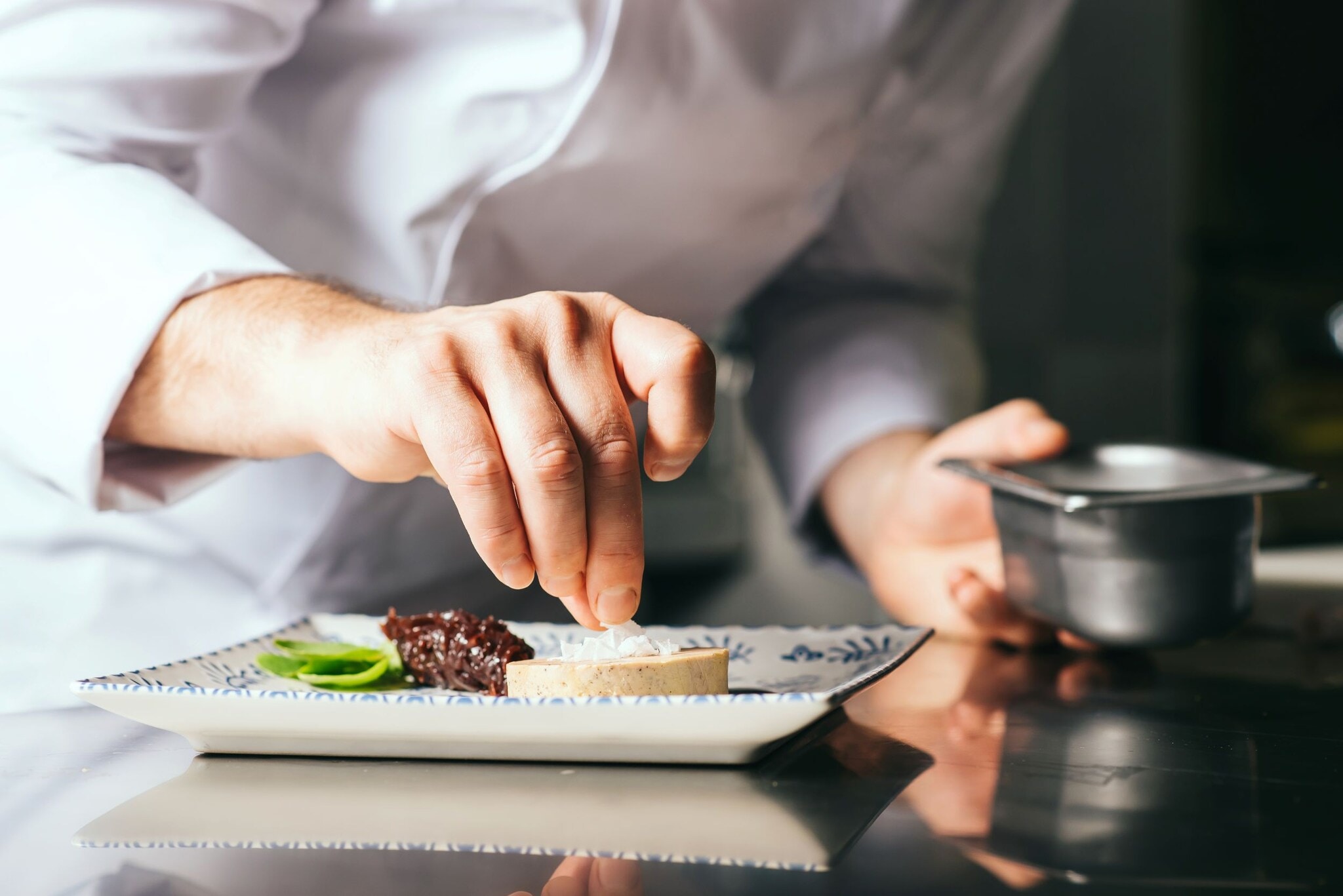 Sternerestaurants-Luxemburg Hand eines Kochs, der einen Teller zubereitet.