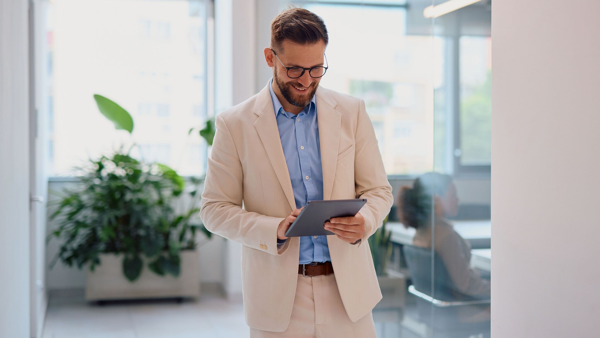 Smiling businessman using digital tablet in modern office Ein gut gewählter Anzug gilt im Berufsleben als Symbol für Status und Seriosität.d und cremefarbenen Anzug bedient ein Tablet heller Büroumgebung.